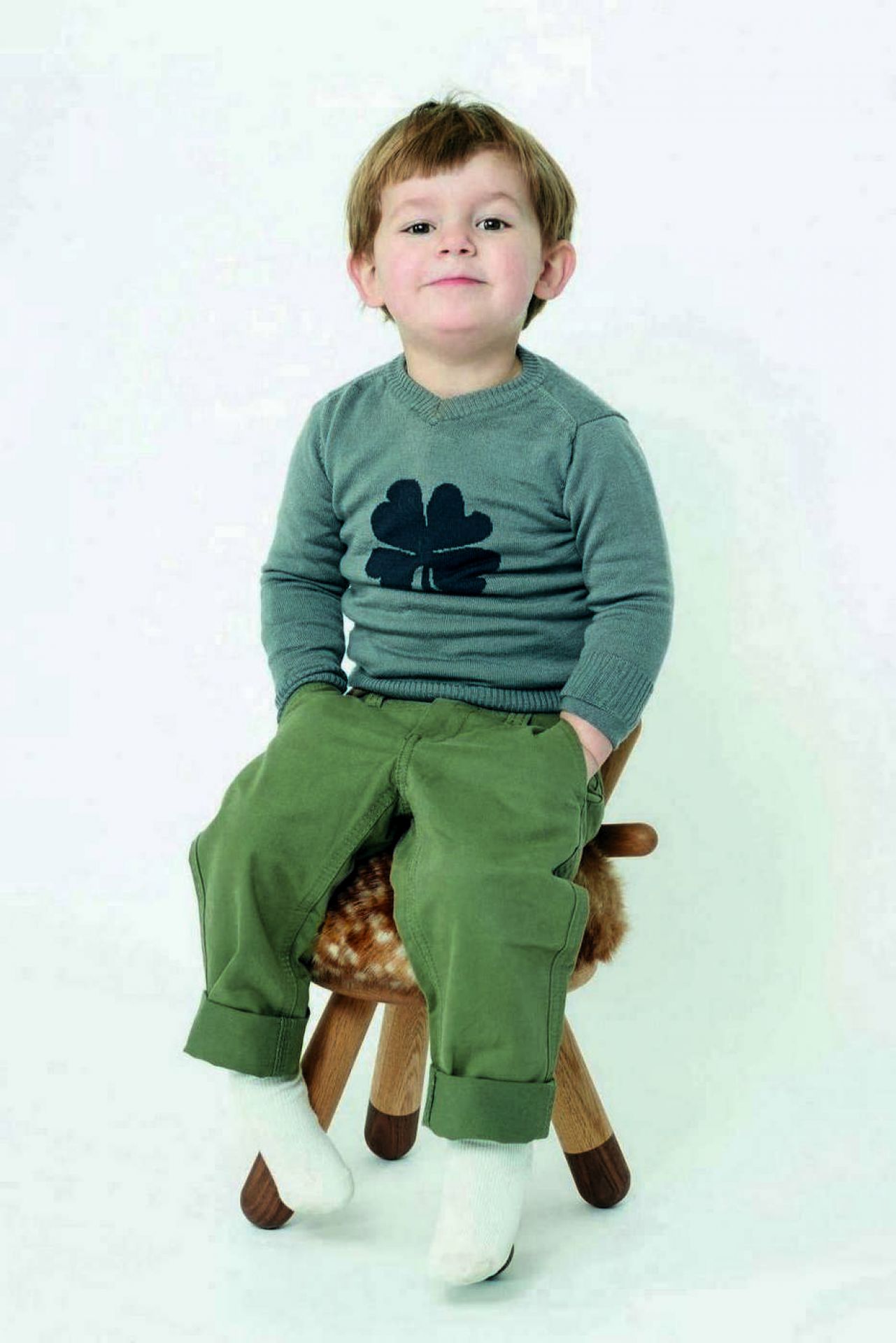 Kleiner Junge sitzt auf einem Bambi Chair Kinderstuhl mit Fellimitat-Sitzfläche vor einem weißen Hintergrund.