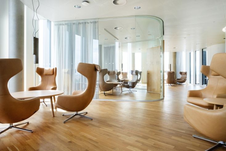 Helle Bürolounge mit mehreren braunen Vitra Grand Repos Sesseln und Holzboden für entspanntes Sitzen.