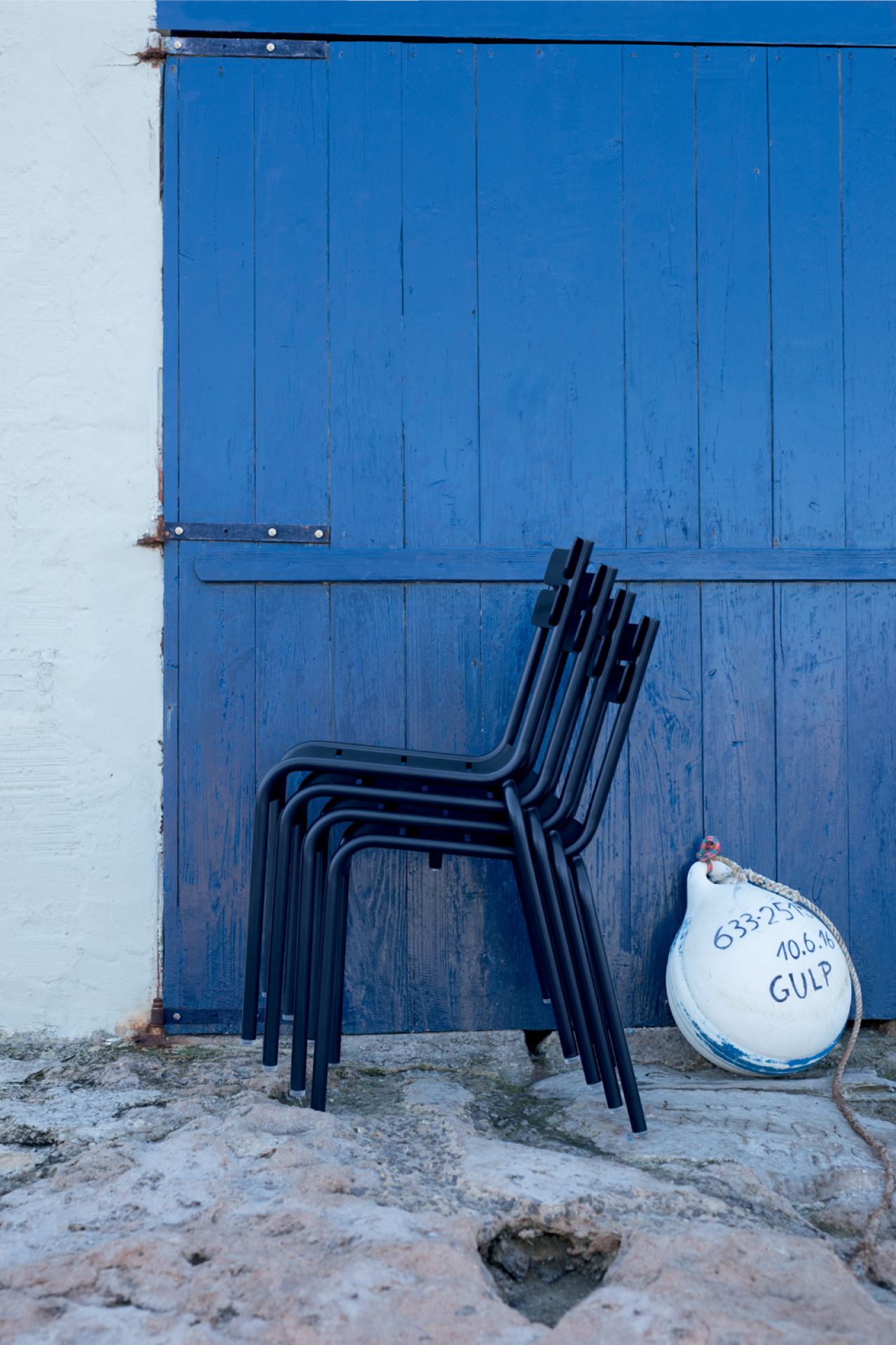 Stapel schwarzkirschfarbener Luxembourg Stühle von Fermob vor einer blauen Holztür, Outdoor-Möbel.