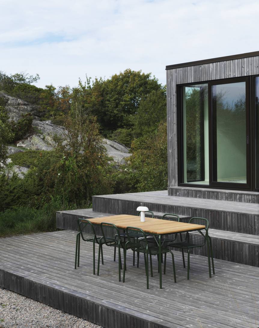 Normann Copenhagen Vig Table Outdoor mit sechs grünen Stühlen auf Holzterrasse vor modernem Haus.