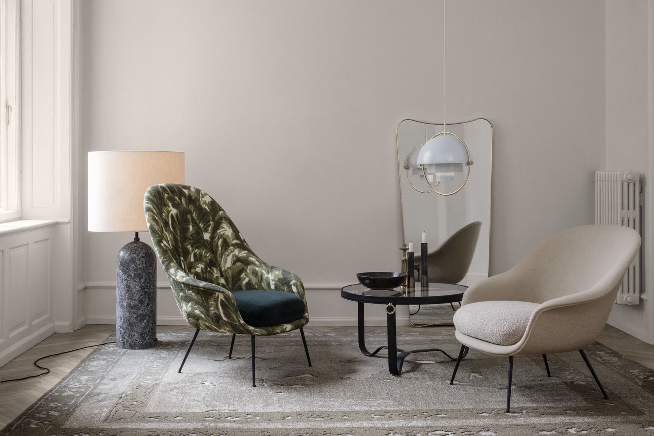 Wohnzimmer mit Gubi Adnet Couchtisch, Sesseln, Lampe und Spiegel in stilvollem Interieur.