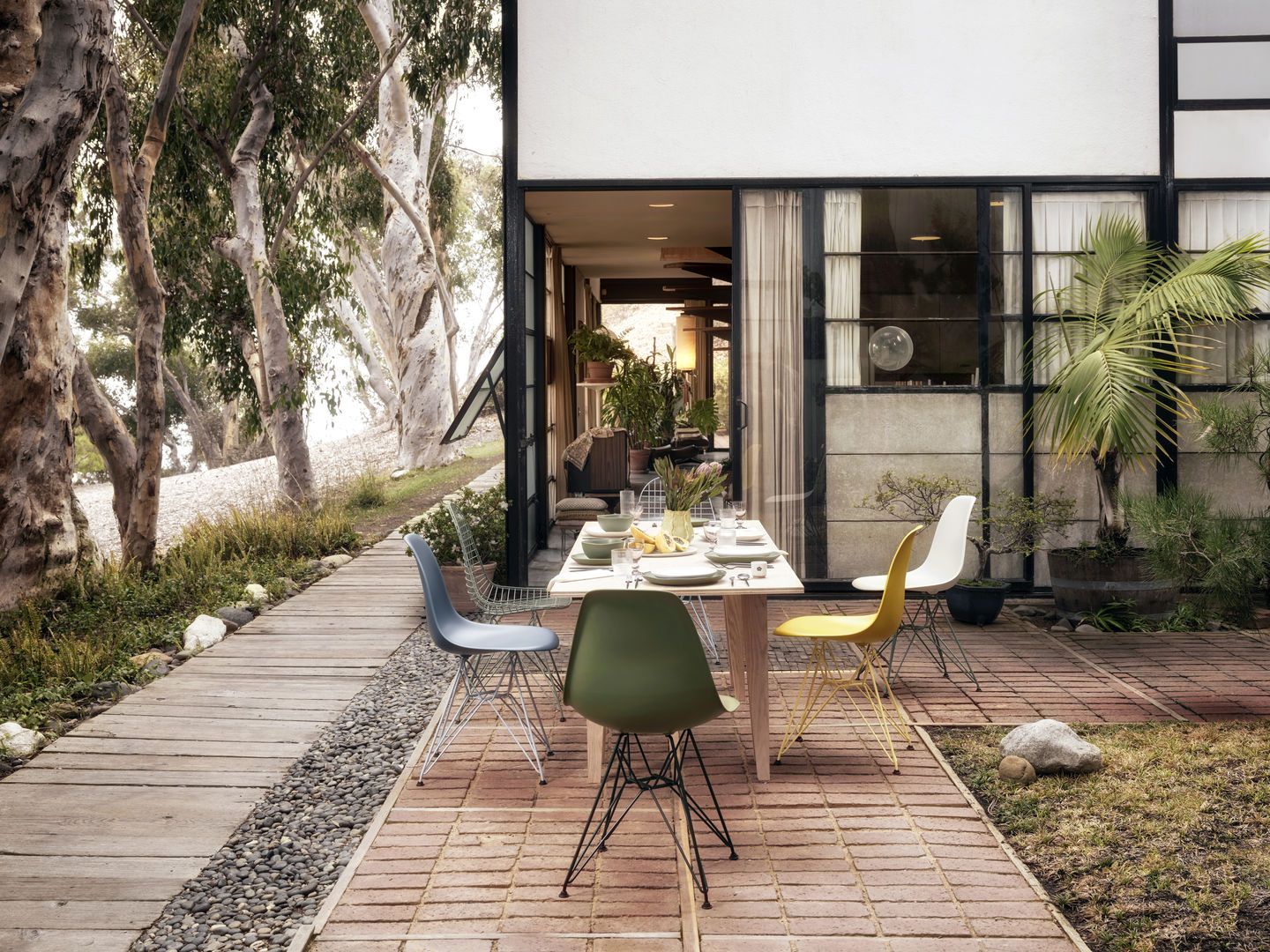Vitra DKR-2 Wire Chair Stühle in verschiedenen Farben an Esstisch im Garten.