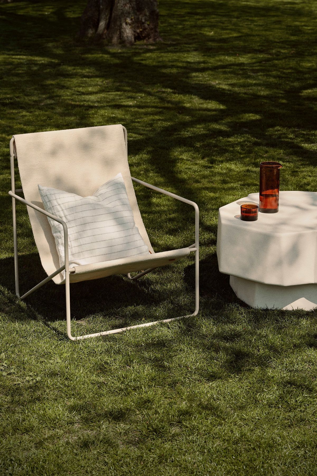 Ferm Living Desert Chair Loungesessel im Garten mit Beistelltisch und Getränken für entspannte Stunden.