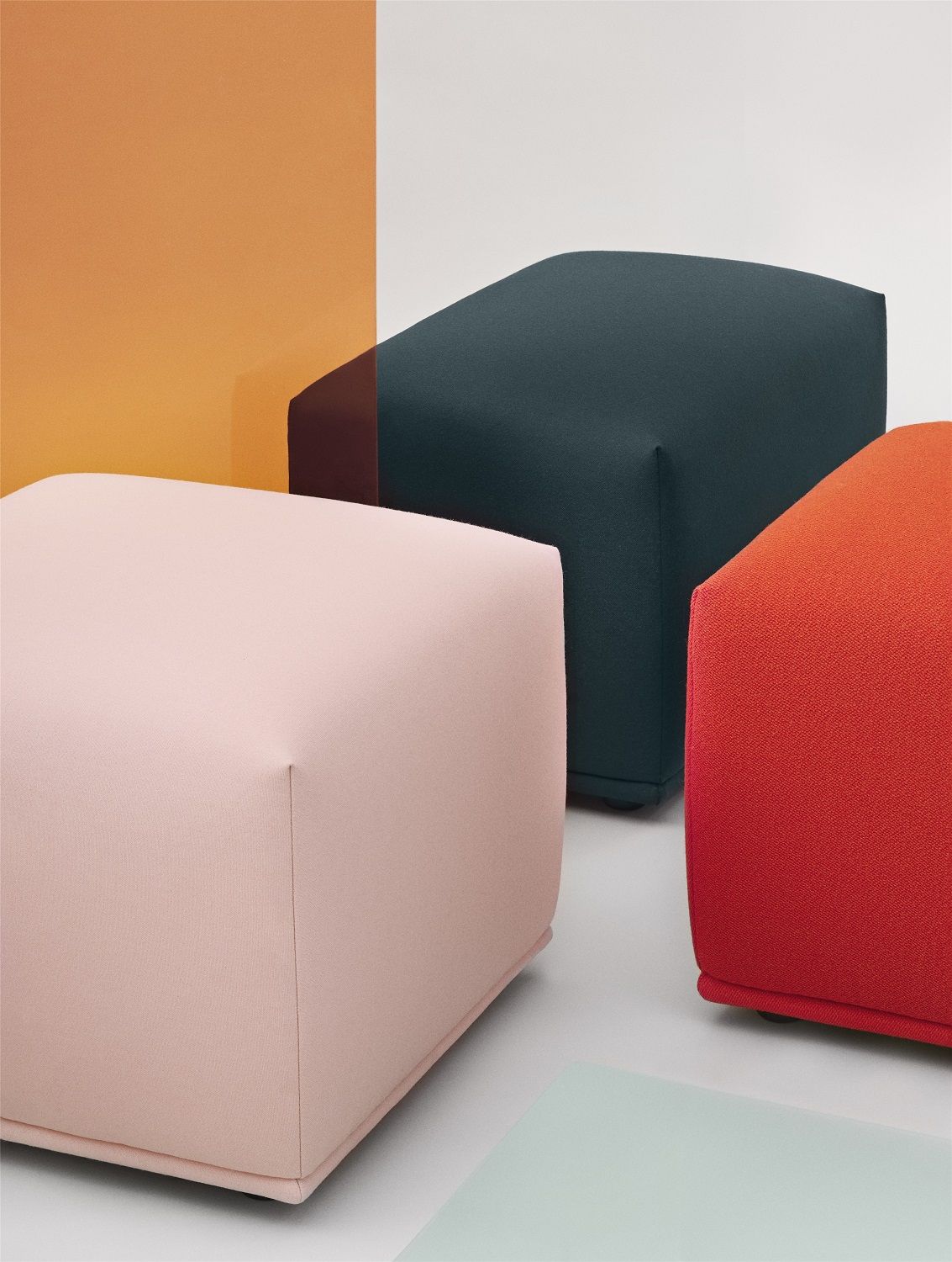 Nahaufnahme von drei Echo Pouf Hockern von Muuto in Rosa, Dunkelblau und Rot. Moderne Sitzmöbel für Wohnzimmer.