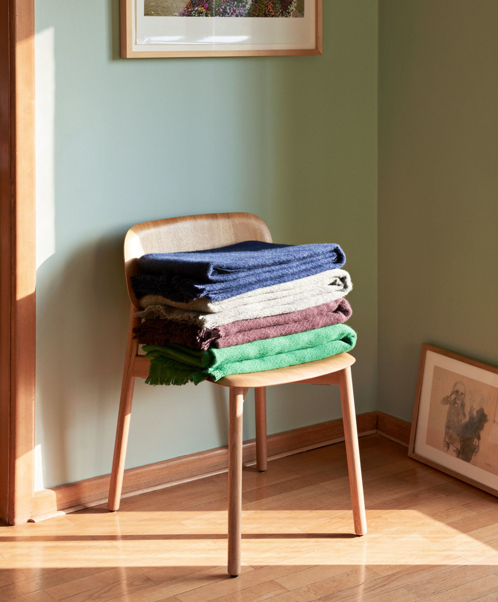 Hay Soft Edge 60 Stuhl aus Holz mit Stapel farbiger Wolldecken im skandinavischen Interieur.