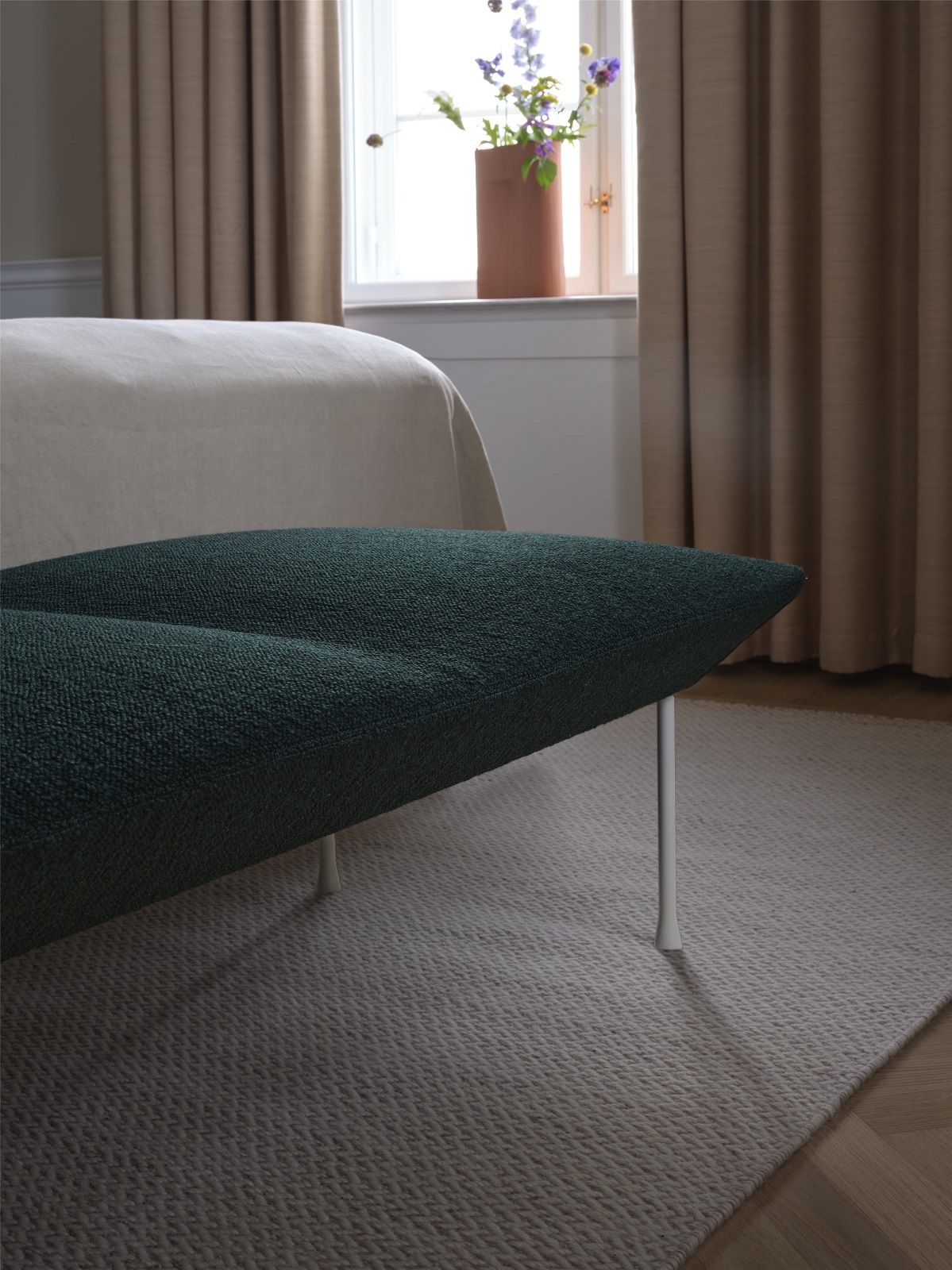 Nahaufnahme der grünen Oslo Bank von Muuto mit weißen Beinen im Schlafzimmer.