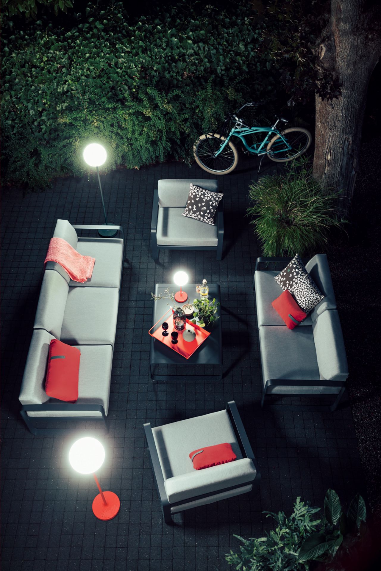 Bellevie Fermob Sessel und Outdoor-Möbel-Set auf dunklem Pflaster mit Beleuchtung und Fahrrad im Hintergrund.