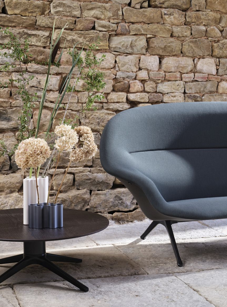 Abalon Table Couchtisch von Vitra neben einem blauen Sessel vor einer Steinwand.