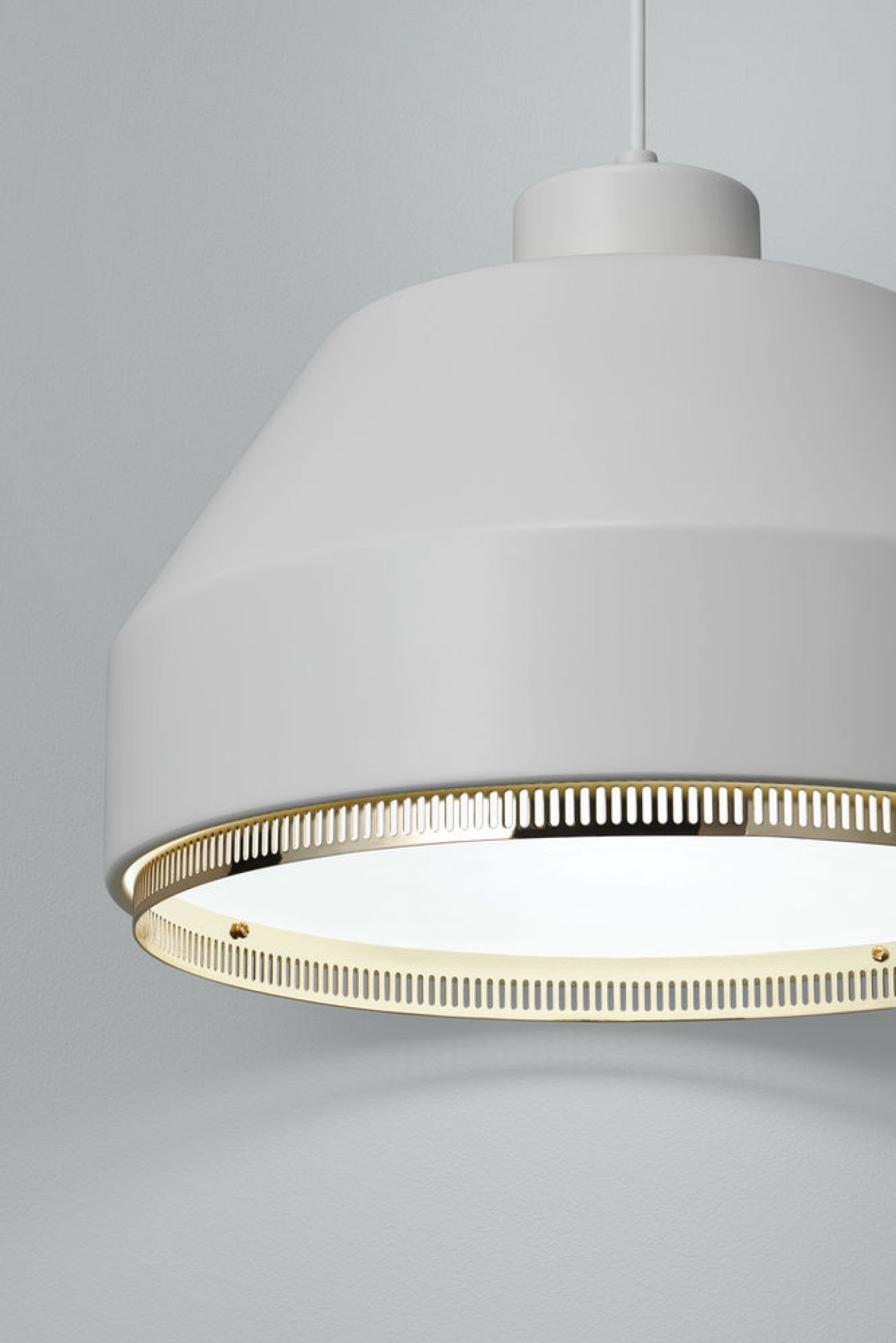 Detailaufnahme der weißen Artek Pendelleuchte AMA500 mit goldfarbenem Akzentring und warmem Licht.