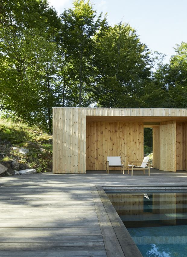 Zwei Pelagus Lounge Sessel von Skagerak by Fritz Hansen auf Holzterrasse neben Pool und Holzhütte.