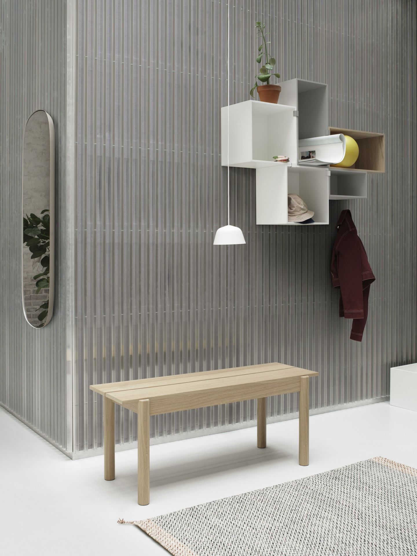 Muuto Mini Stacked Regalsystem 2.0, weiße und holzfarbene Module an grauer Wand, Bank und Spiegel.
