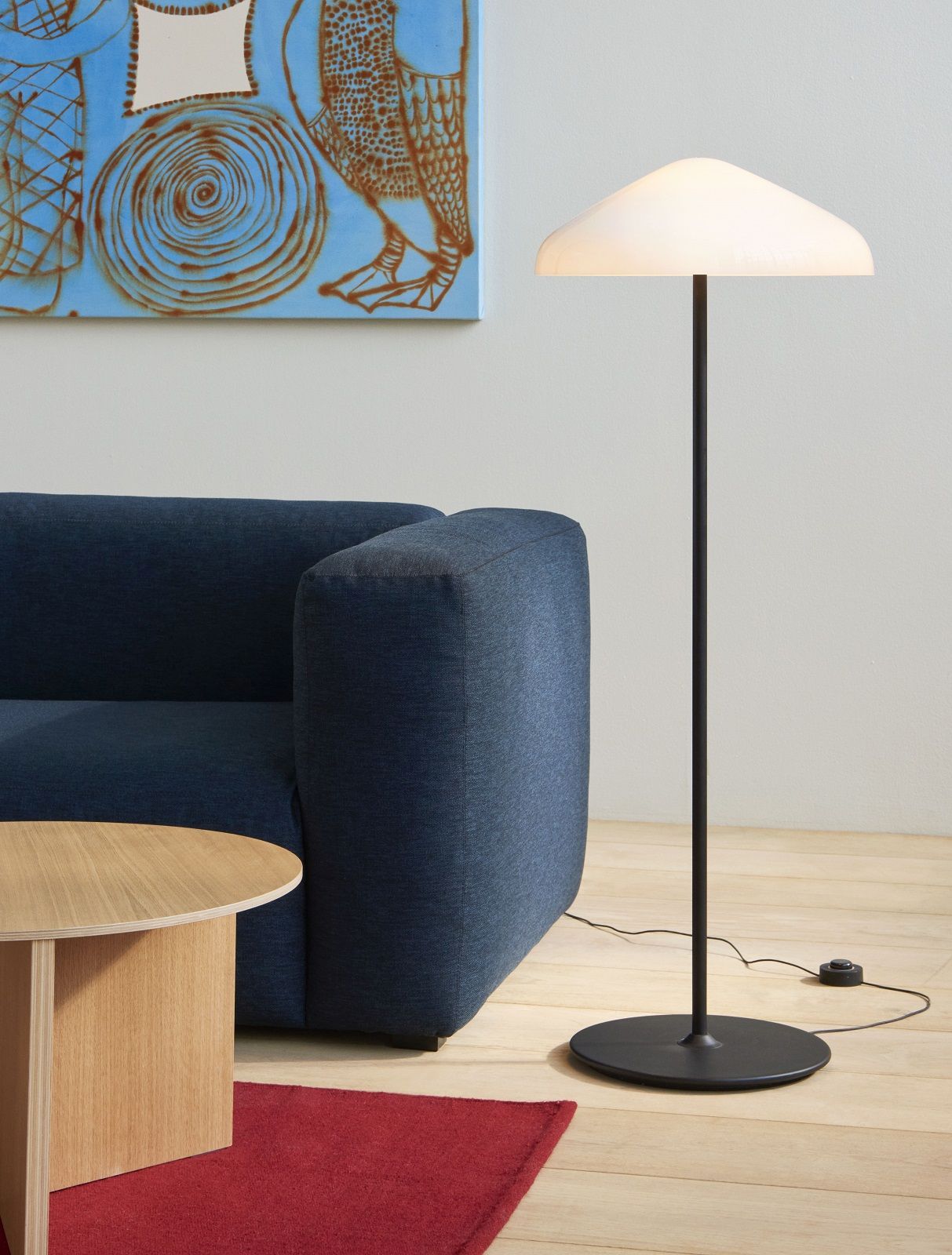 Hay Slit Table Wood Round XL Beistelltisch aus Eichenholz neben einem blauen Sofa und einer Stehlampe.