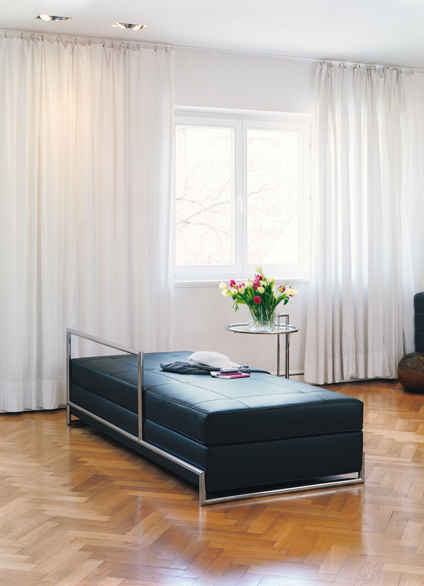 ClassiCon E1027 Adjustable Table Beistelltisch im Wohnzimmer mit schwarzer Liege und Tulpenstrauß.