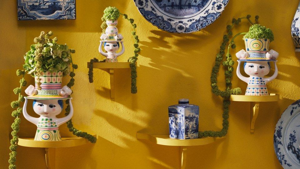 Detailaufnahme von drei Bjorn Wiinblad Lady with Hat Vasen auf gelben Regalen mit grünen Pflanzen.