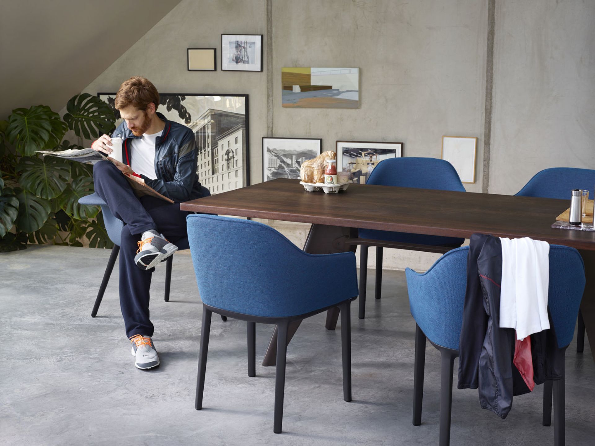 Blauer Organic Conference Stuhl von Vitra an einem Esstisch mit lesendem Mann.