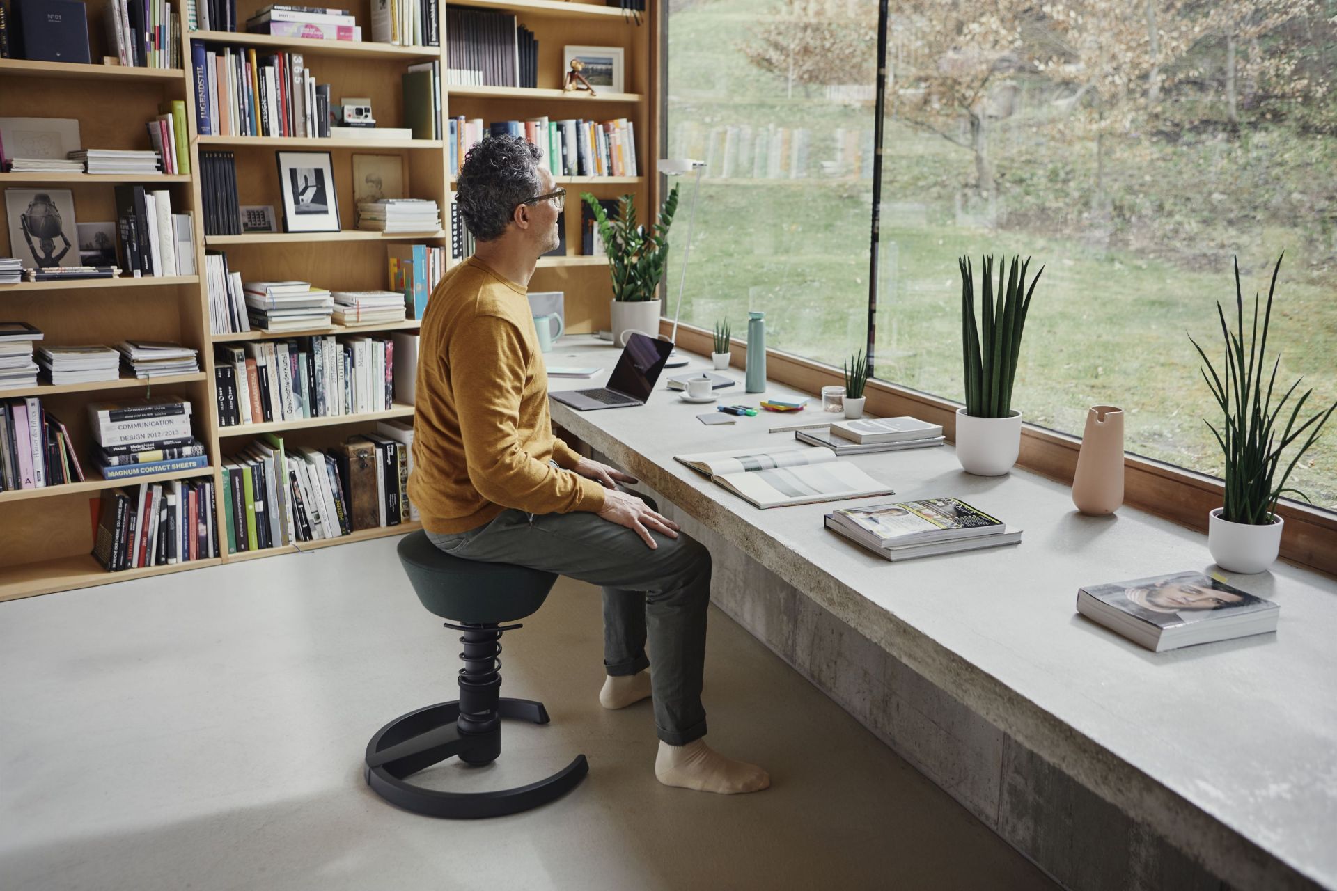 Mann sitzt auf ergonomischem Swopper Bürostuhl am Schreibtisch mit Laptop und Pflanzen vor Fenster.