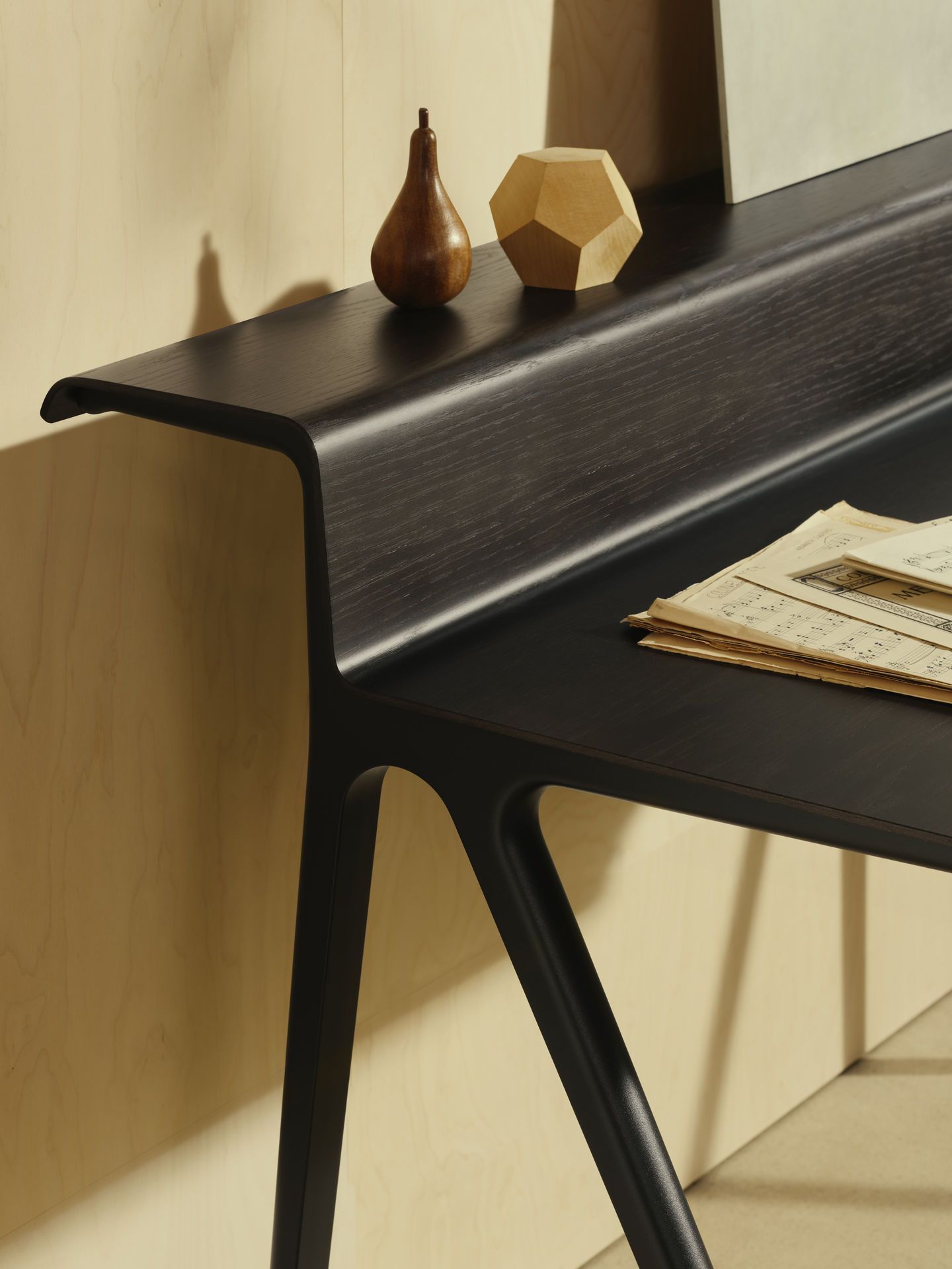Detailaufnahme des schwarzen Courier Schreibtischs von Vitra mit Holzobjekten und Notenblättern. Moderner Bürotisch für Arbeitszimmer.