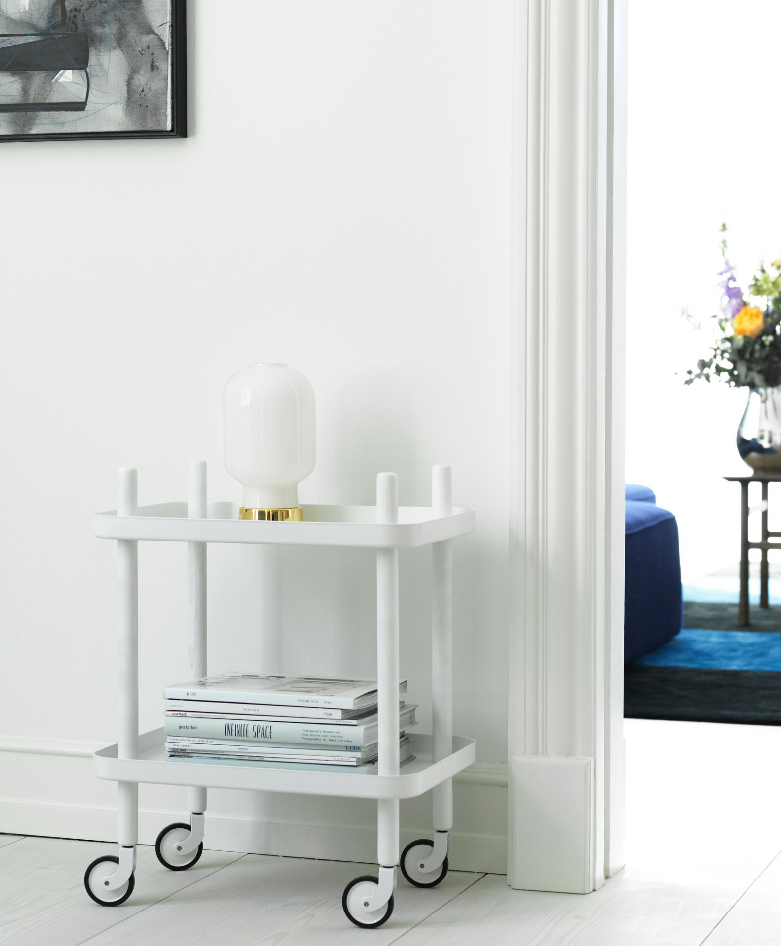 Weißer Normann Copenhagen Block Table Servierwagen mit Lampe und Zeitschriften in hellem Flur.