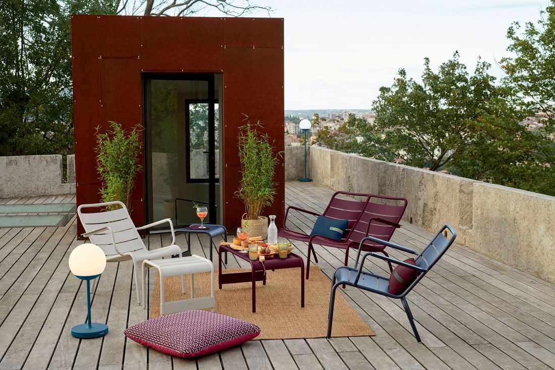 Luxembourg Lounge Sessel Outdoor von Fermob auf einer Dachterrasse mit weiteren Gartenmöbeln und Dekoration.