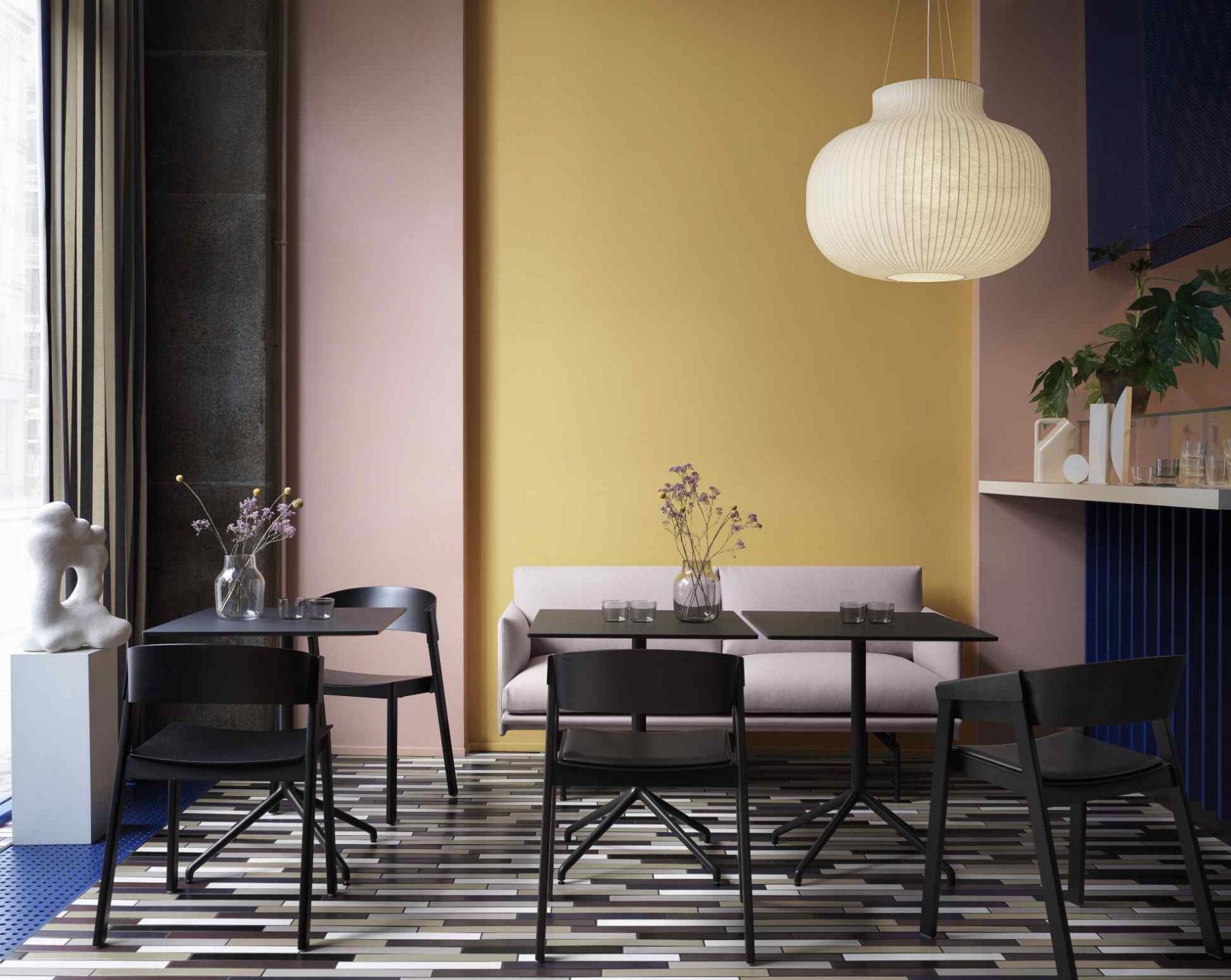 Helle Muuto Strand Pendelleuchte über Esstisch mit schwarzen Stühlen in modernem Interieur.