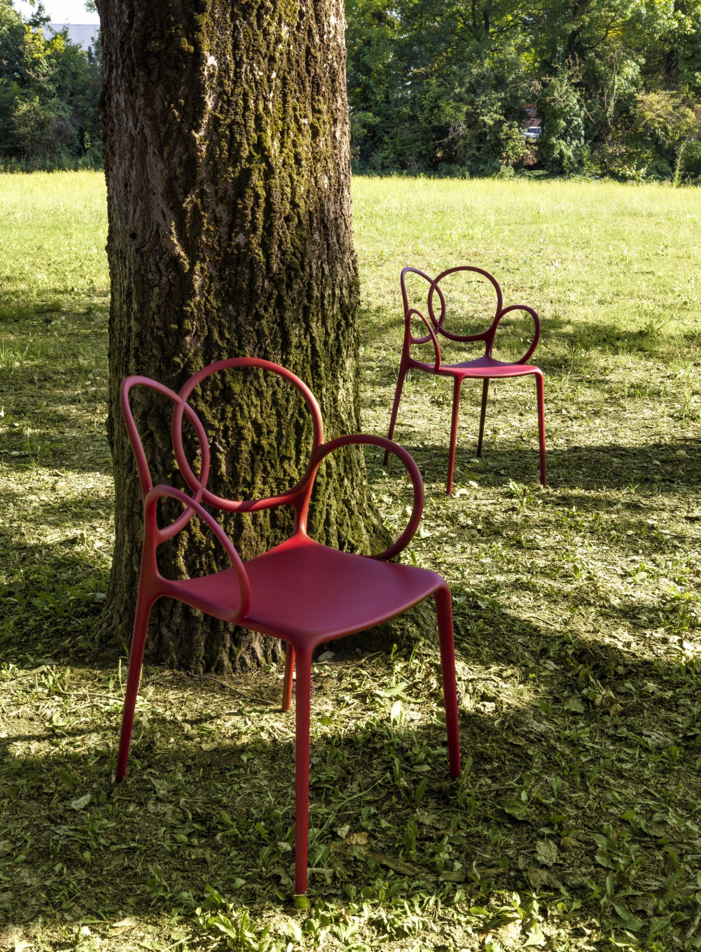Zwei rote Sissi Armlehnstühle von Driade im Garten, moderne Outdoor Sitzmöbel.