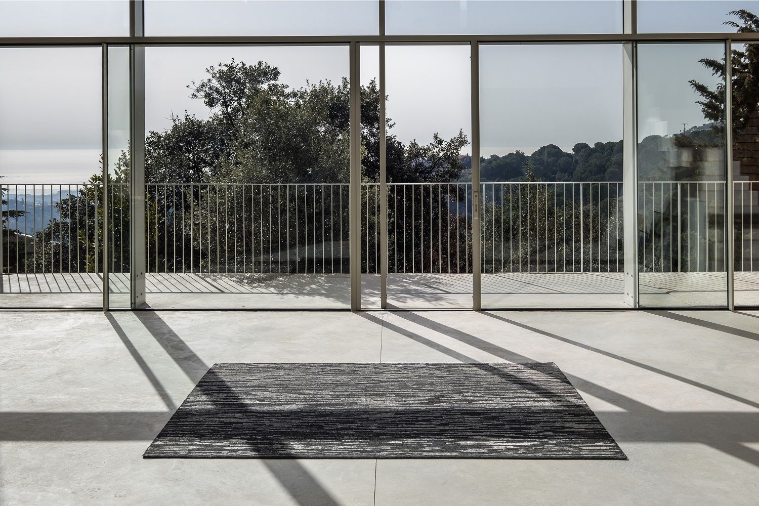 Nanimarquina Doblecara Rug Teppich in Grau vor Panoramafenster mit Blick auf die Natur.