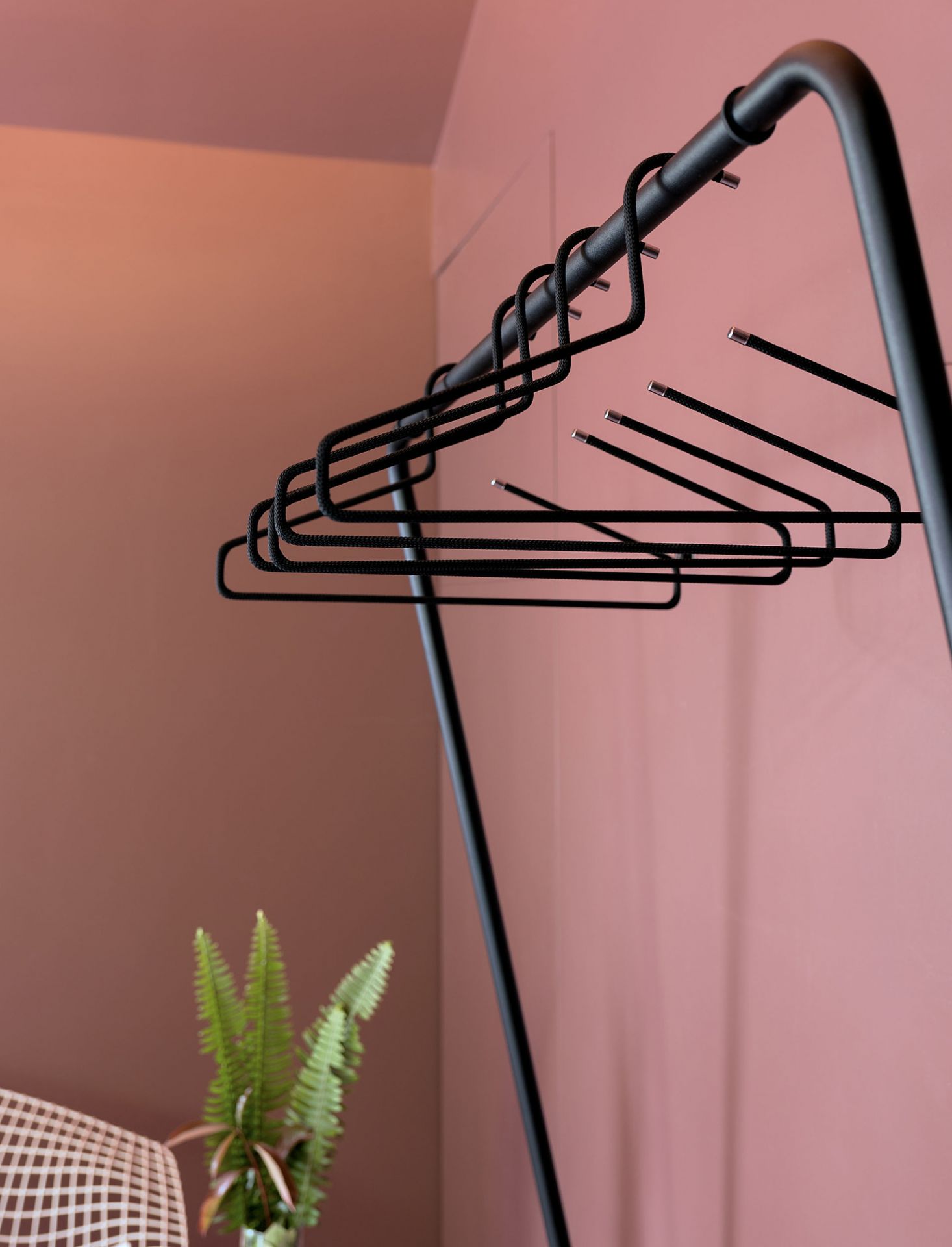 Schwarze Curve Wandgarderobe von Schönbuch mit Kleiderbügeln vor rosa Wand, minimalistisches Design für Flur und Eingangsbereich.