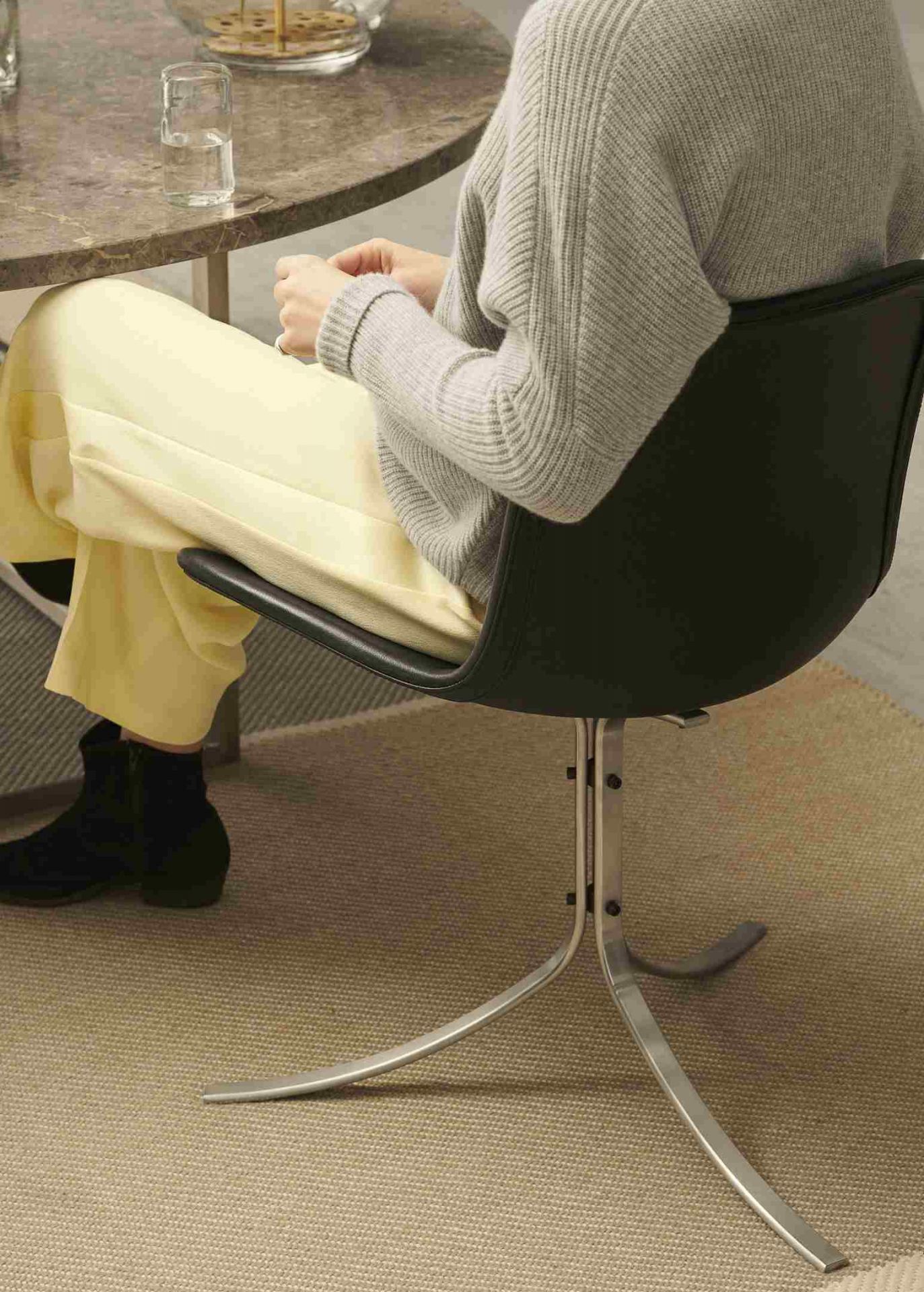 Person sitzt auf einem schwarzen PK9 Stuhl von Fritz Hansen am Esstisch.
