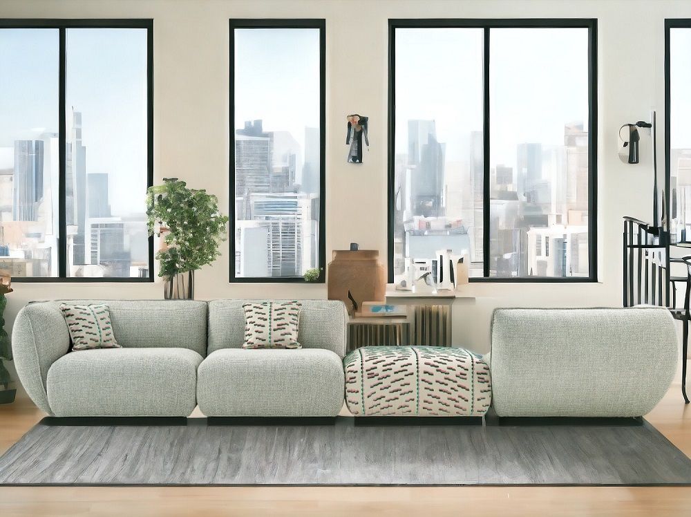Helles Mia Modulsofa von Freifrau Manufaktur mit Kissen und Hocker vor Fensterfront mit Skyline.