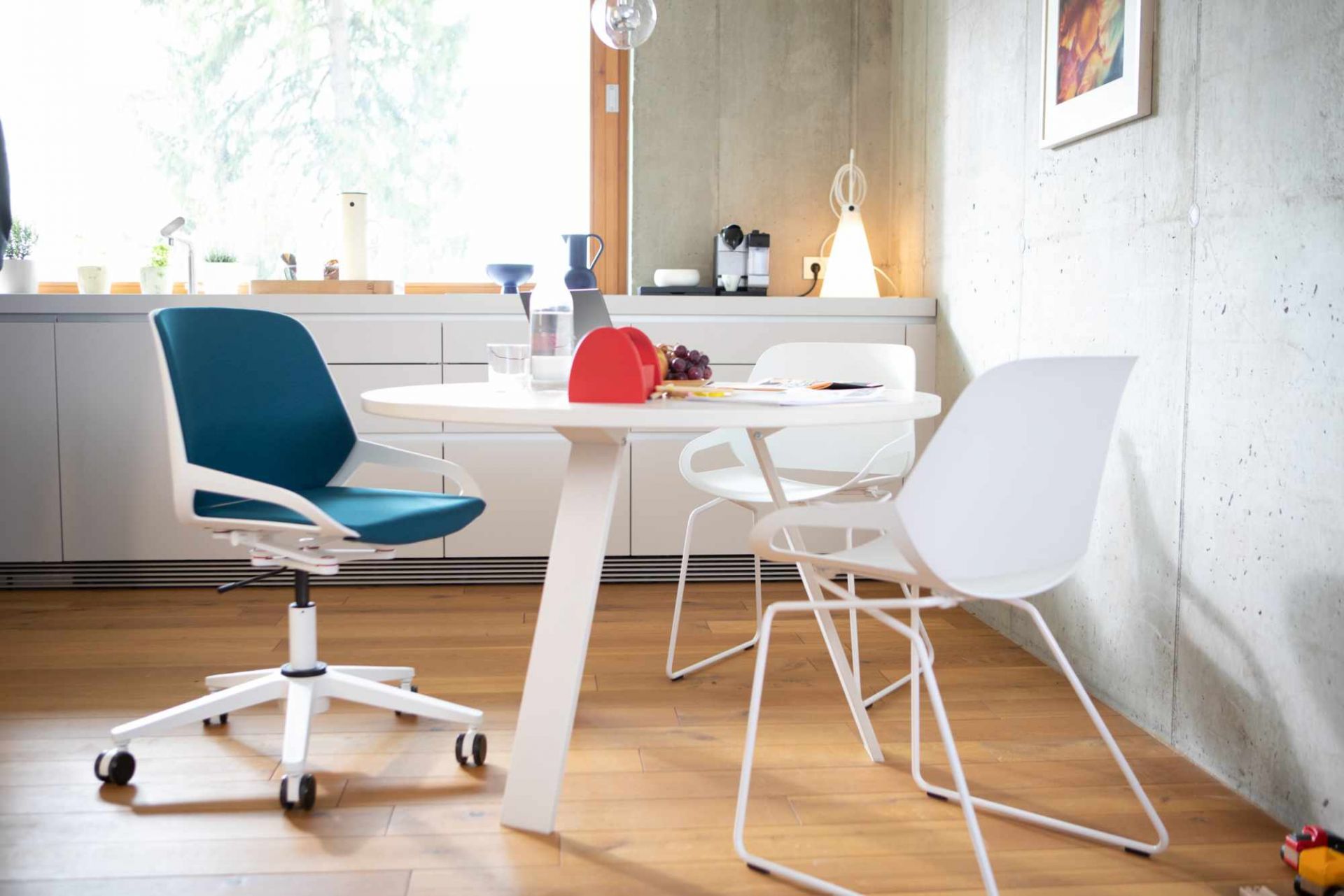 Numo Task Bürodrehstuhl von Aeris mit blauem Sitz und weißem Gestell am Esstisch im modernen Büro.