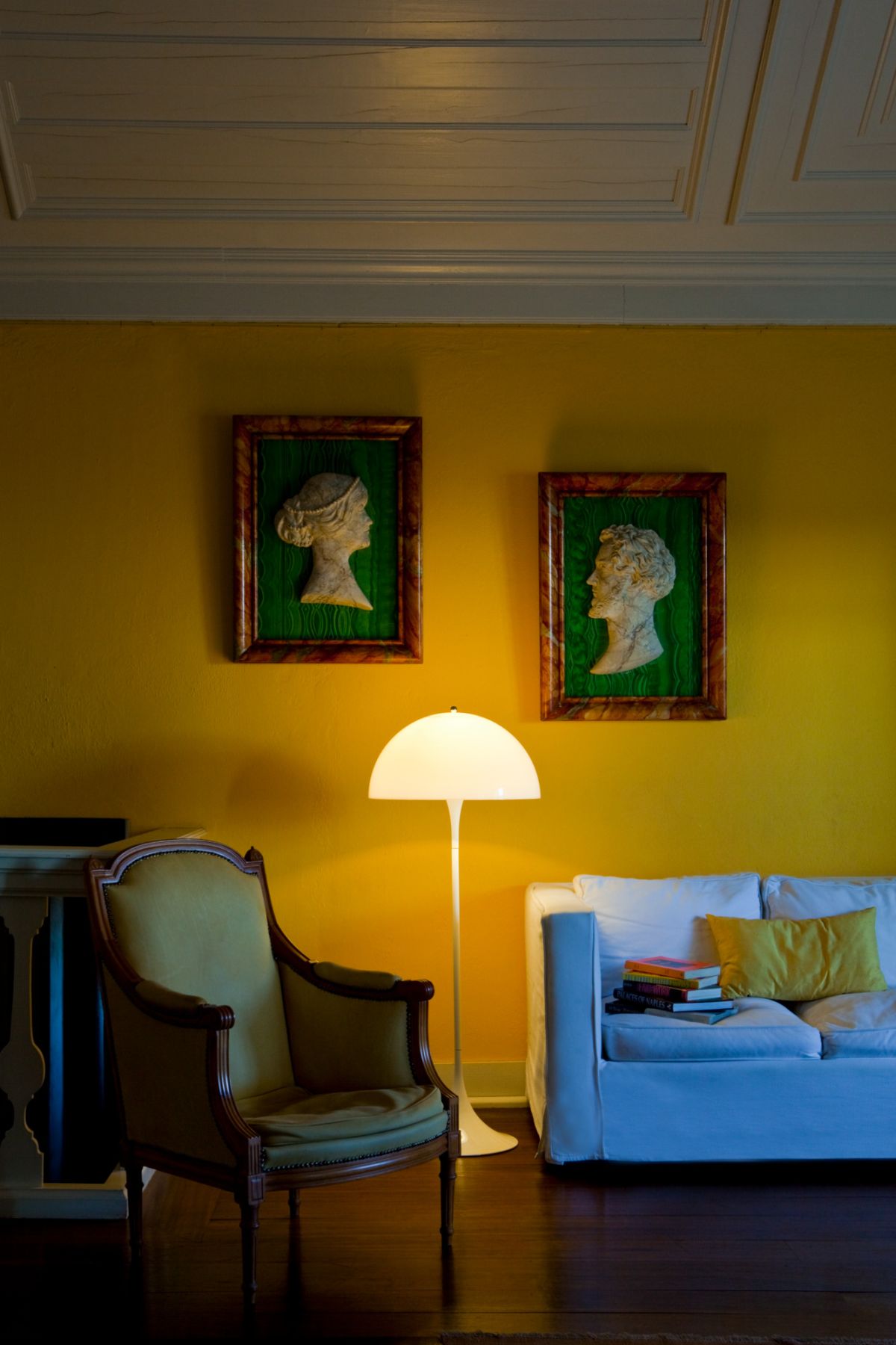 Gelbes Wohnzimmer mit Sessel, Sofa, Stehlampe und gerahmten Porträt-Reliefs als Wanddeko für stilvolles Wohnen.