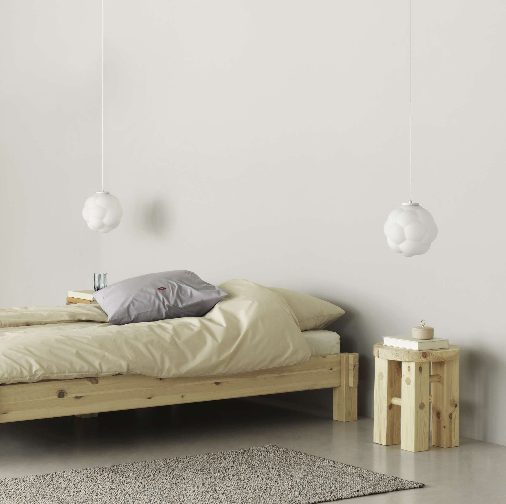 Zwei Bubba Pendelleuchten von Normann Copenhagen über einem Bett und einem Holzhocker im Schlafzimmer.