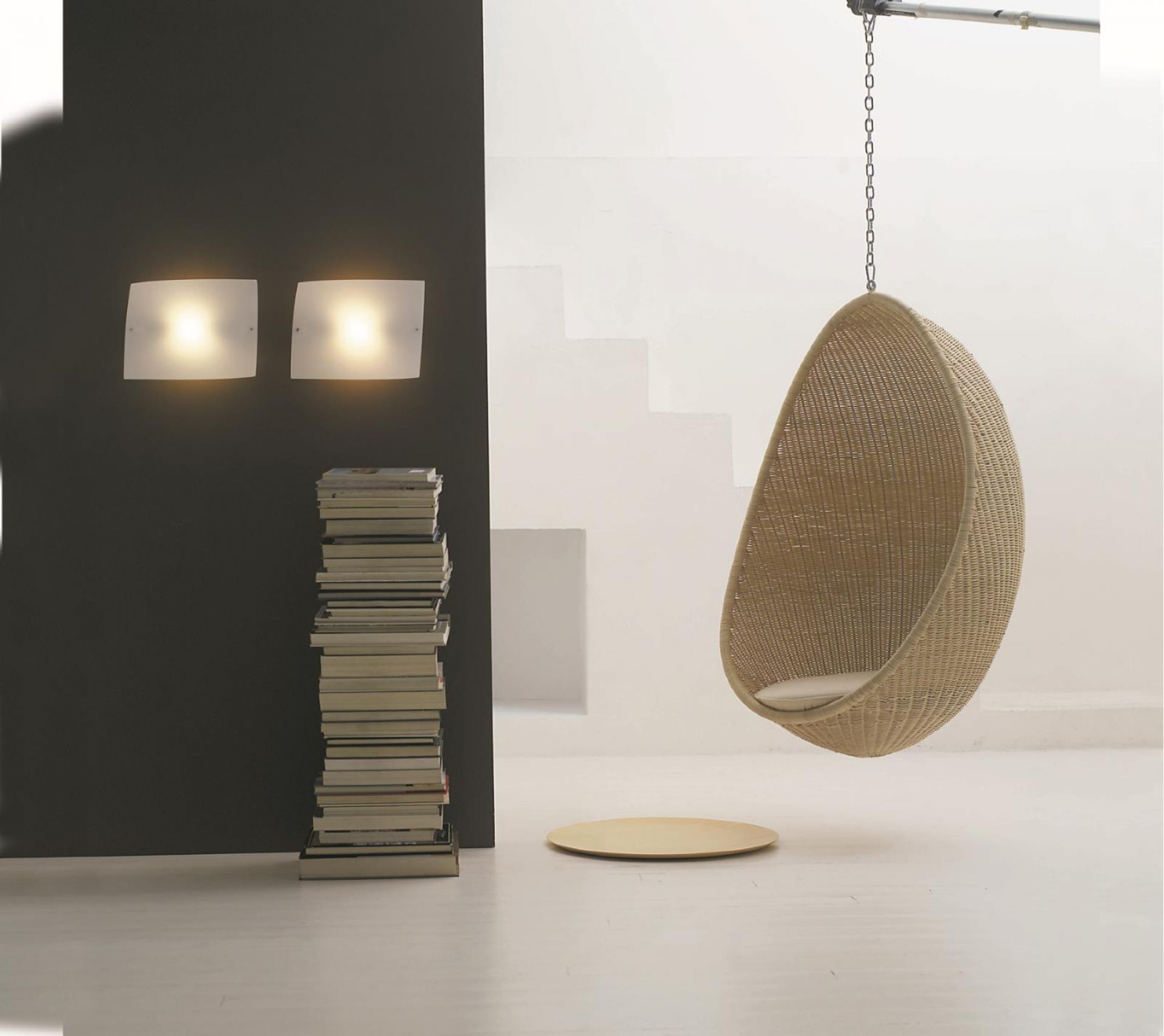 Zwei quadratische Foscarini Wandleuchten neben einem Bücherstapel und einem Hängesessel in einem hellen Raum.