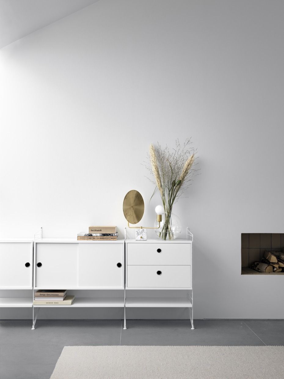Weißes String Regal mit Schiebetüren und Schubladen im Wohnzimmer, dekoriert mit Lampe und Vase.