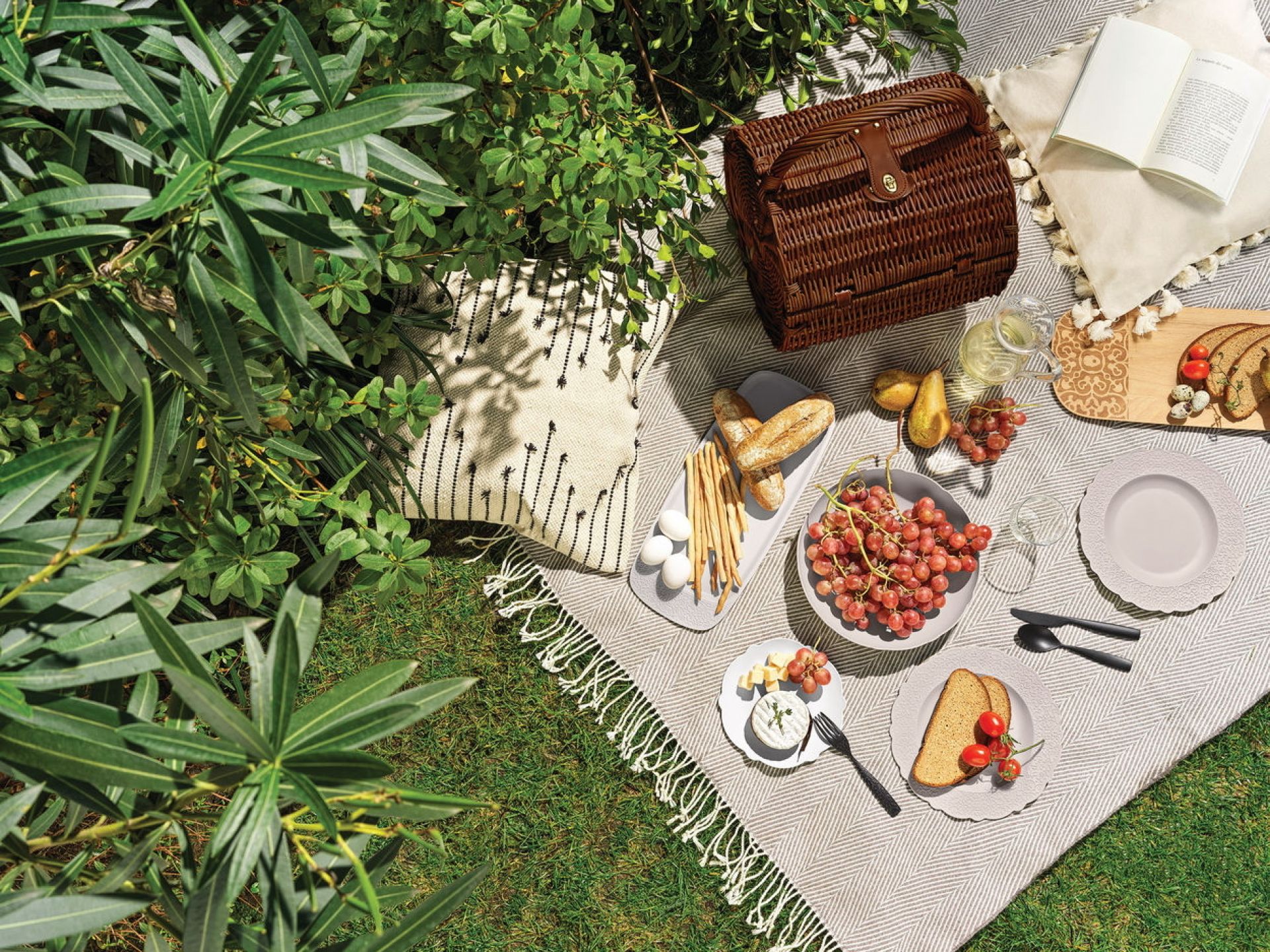 MW75 Picknickkorb von Alessi mit Geschirr und Speisen auf einer Decke im Grünen.