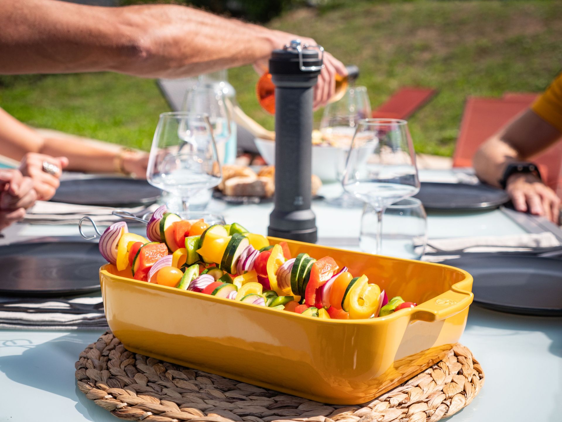 BBQ Szene mit Peugeot Pfeffermühle: Grillspieße mit Gemüse in gelber Schale, Outdoor-Barbecue.
