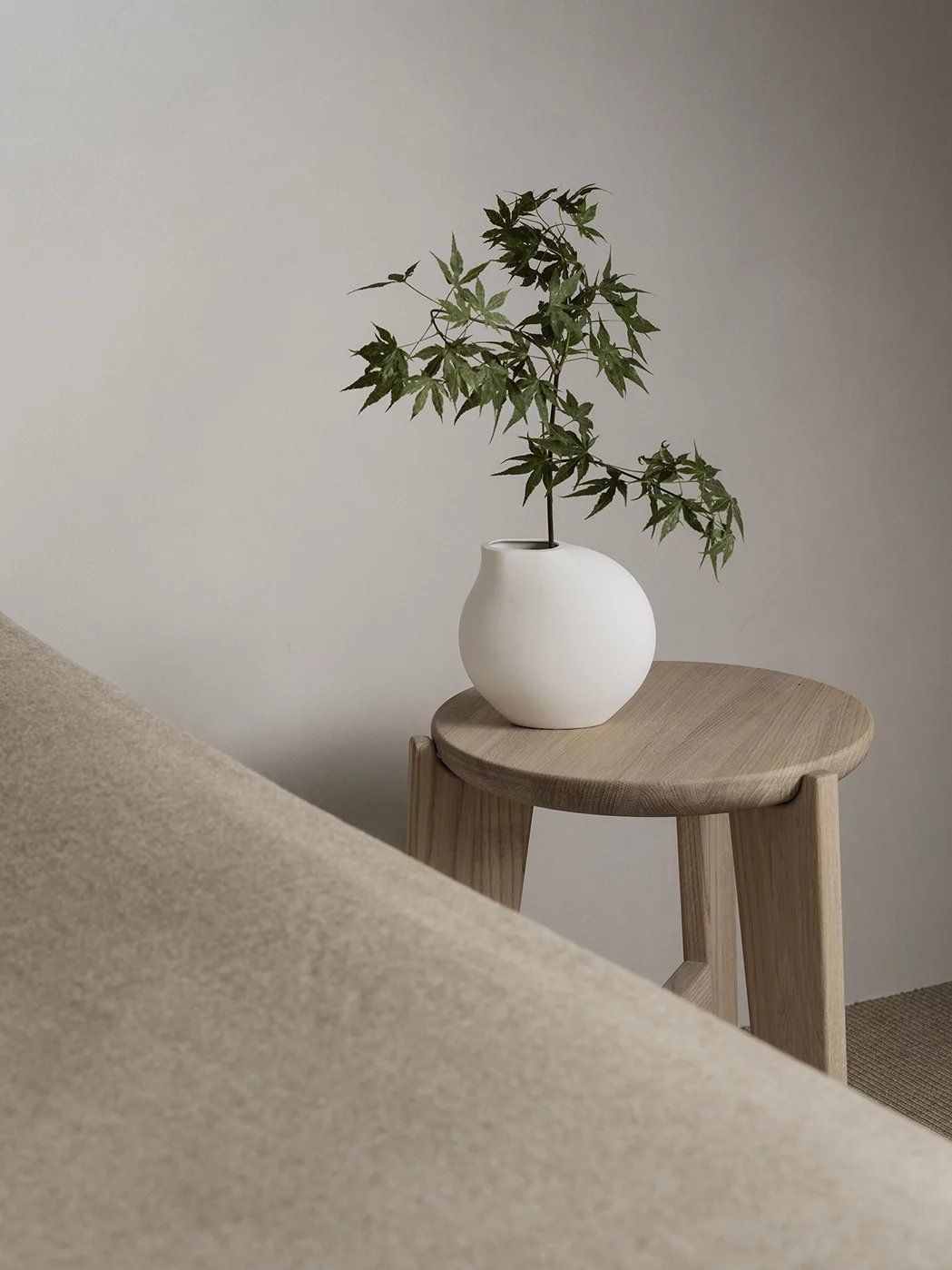 Eli Hocker von Blomus: Runder Sitzhocker aus hellem Holz mit Pflanze in Vase.