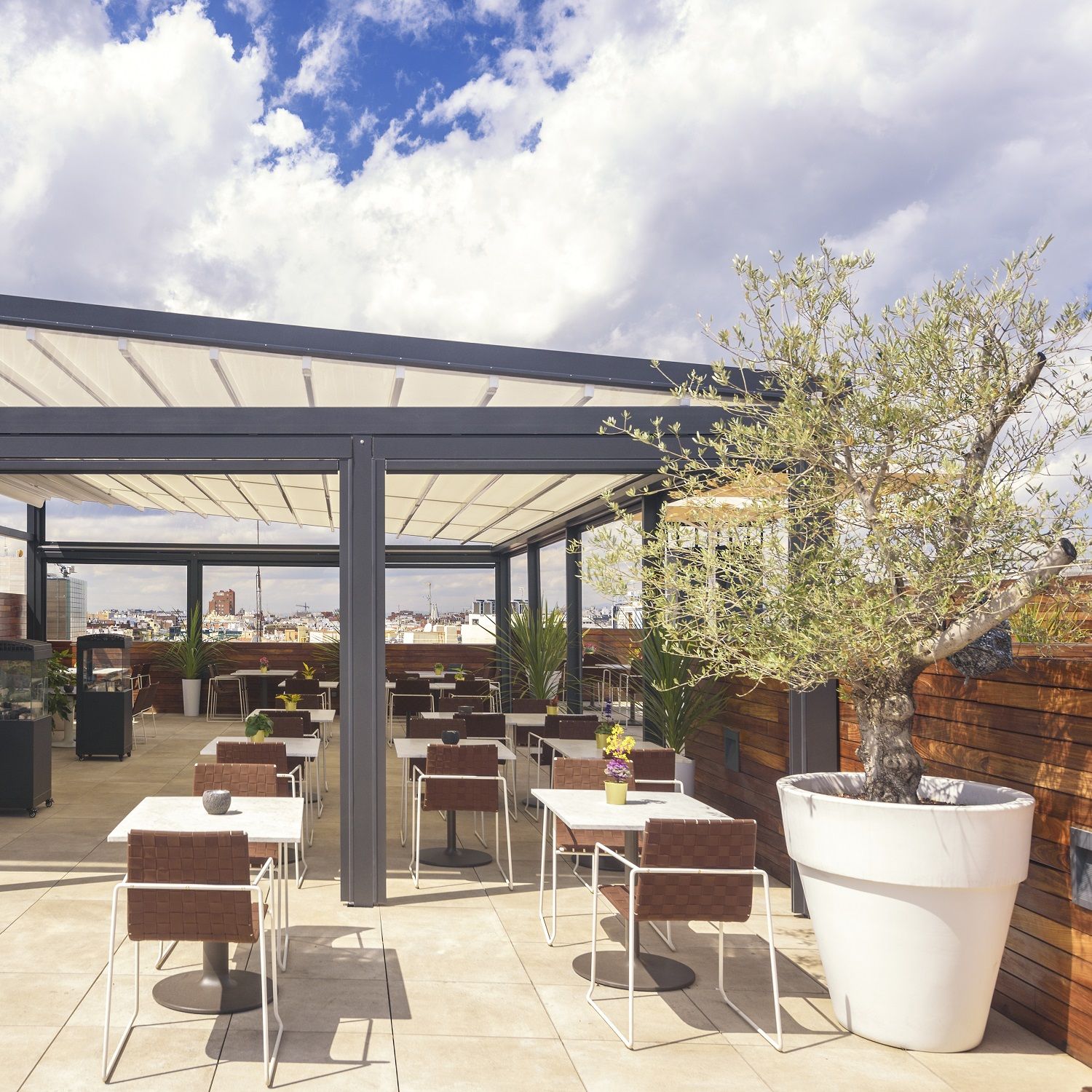 Andreu World Trenza Armlehnenstuhl SO0700 auf einer Dachterrasse mit Tischen und Stühlen unter einem Sonnendach.