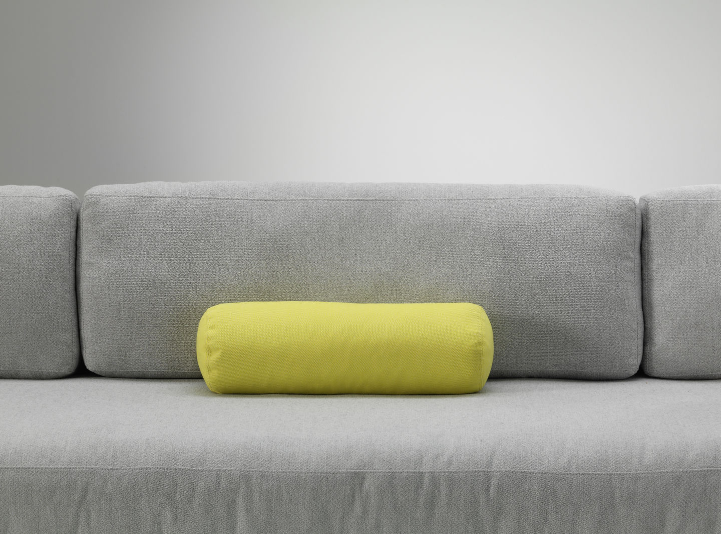 Vitra Kissen: Gelbes, zylinderförmiges Sofakissen auf einem grauen Sofa, modernes Wohnaccessoire für stilvolles Interieur.