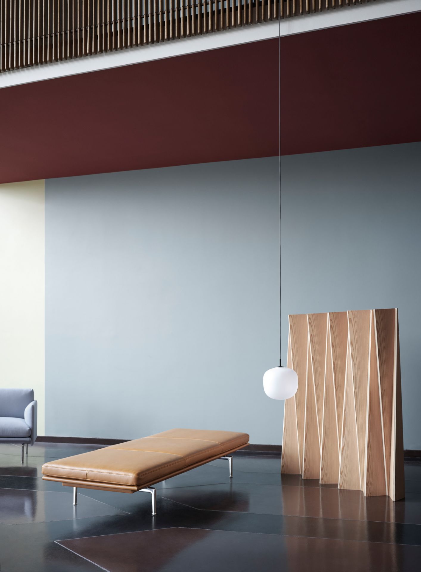 Moderne Raumgestaltung mit Rime Pendelleuchte von Muuto in Grau, kombiniert mit Ledercouch und Holzpaneel.