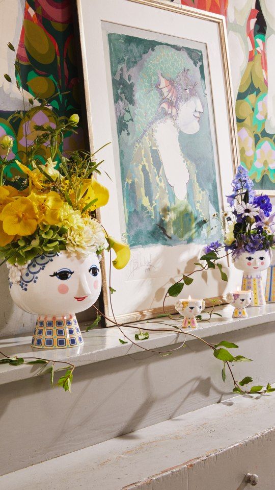 Dekoratives Arrangement mit Bjorn Wiinblad Eva Teelichthaltern und Vasen mit Blumenschmuck auf einem Kaminsims.
