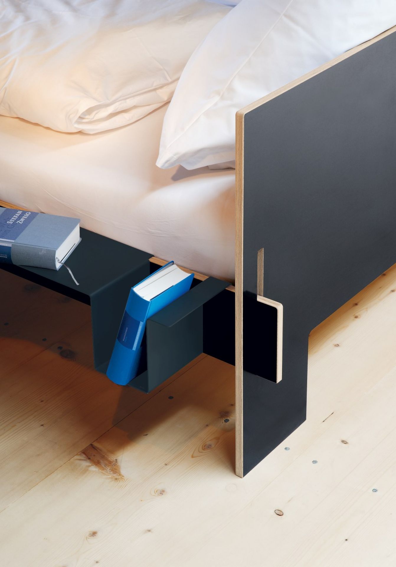 Anthrazitfarbene Seitenablage für Siebenschläfer Bett von Moormann mit Büchern auf hellem Holzboden.