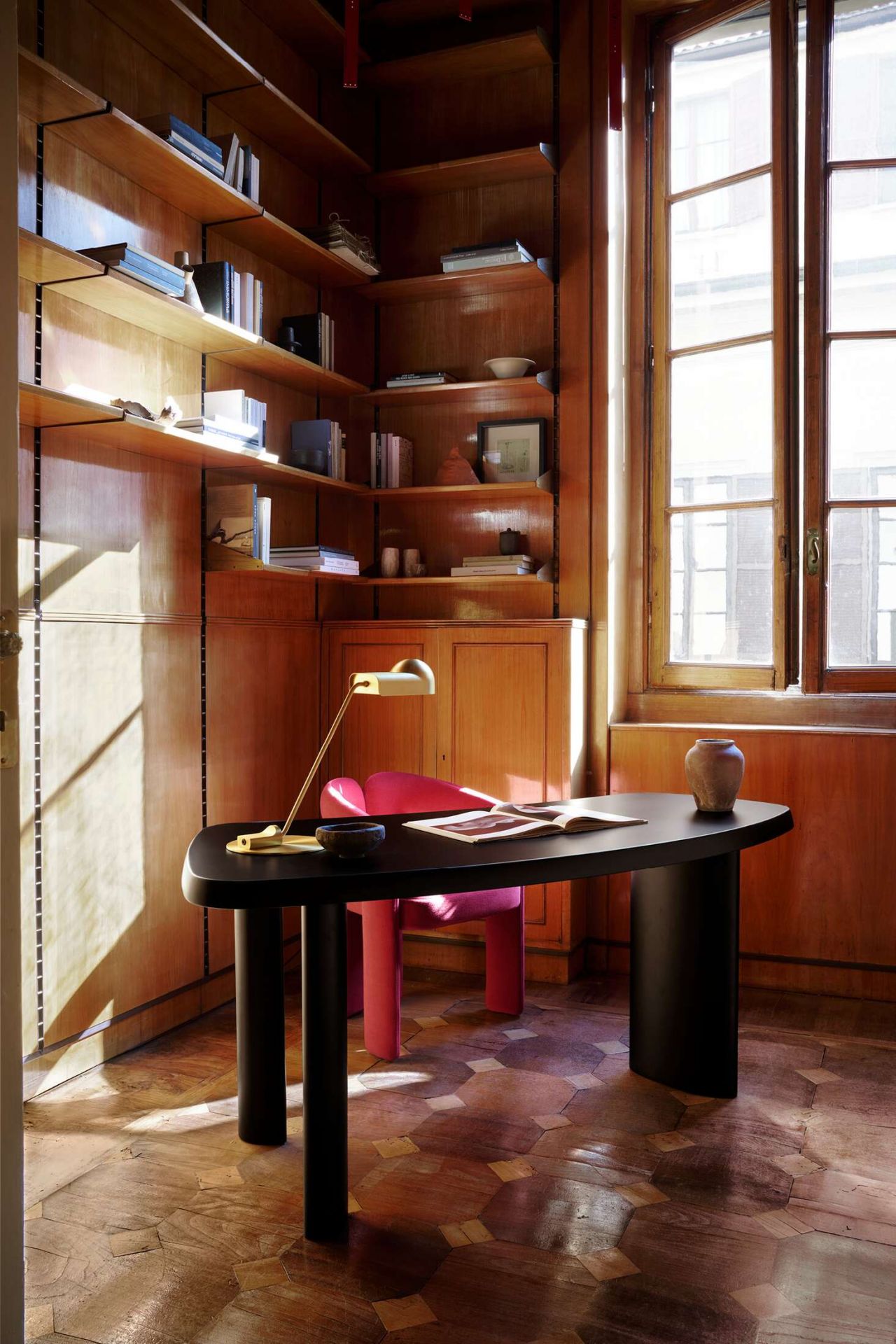 Innenaufnahme mit Schreibtisch, Lampe und rosafarbenem 562 Dudet Sessel von Cassina in einem Arbeitszimmer mit Holzvertäfelung.