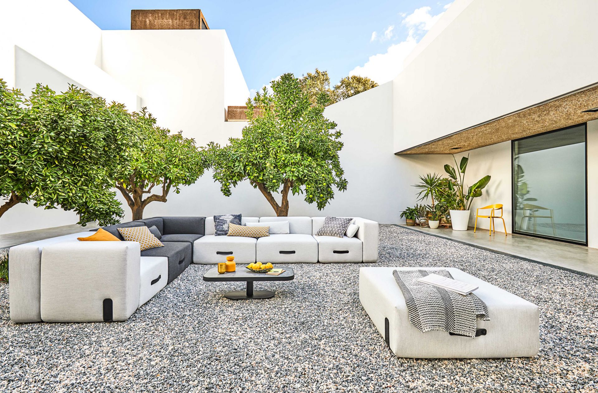 Miami Outdoor Sofa Lounger Conmoto auf Kiesterrasse mit Beistelltisch, Obstschale und mediterranen Pflanzen.