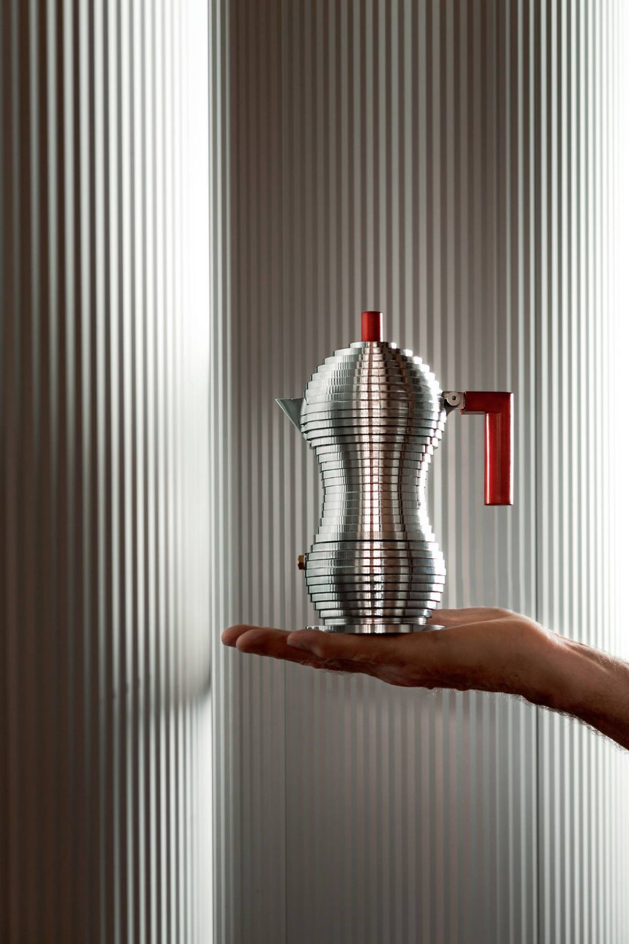 Alessi Pulcina Espressokocher MDL02 auf einer Handfläche, modernes Design, silberfarben mit rotem Griff.