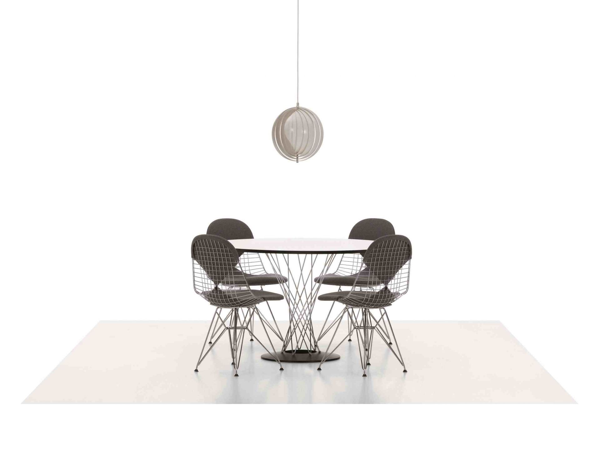 Vitra Noguchi Dining Table mit vier Wire Chairs und einer Hängelampe auf hellem Teppich.