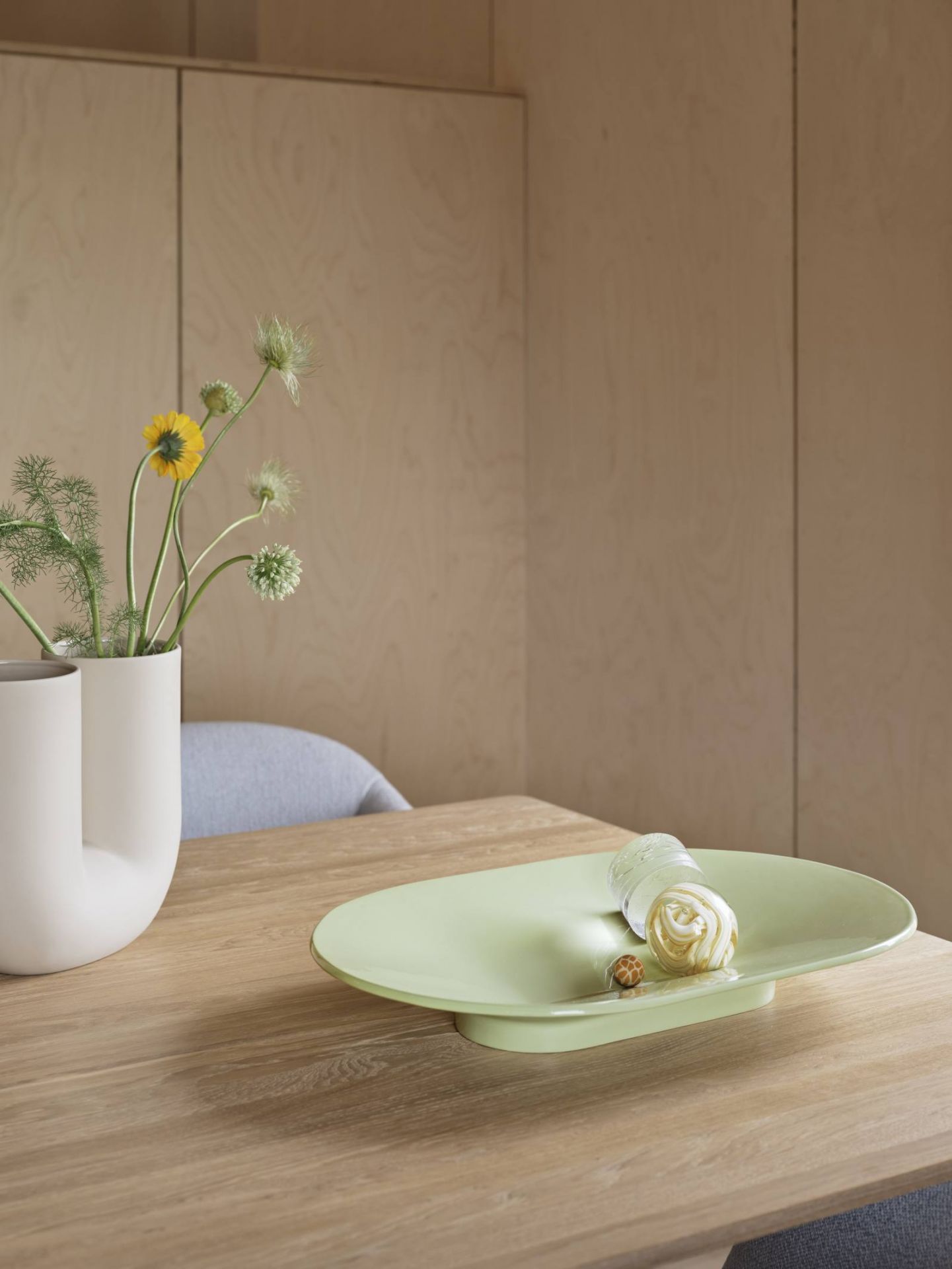 Nahaufnahme eines Muuto Fiber Armlehnstuhls mit Blumen und dekorativer Schale auf einem Holztisch.
