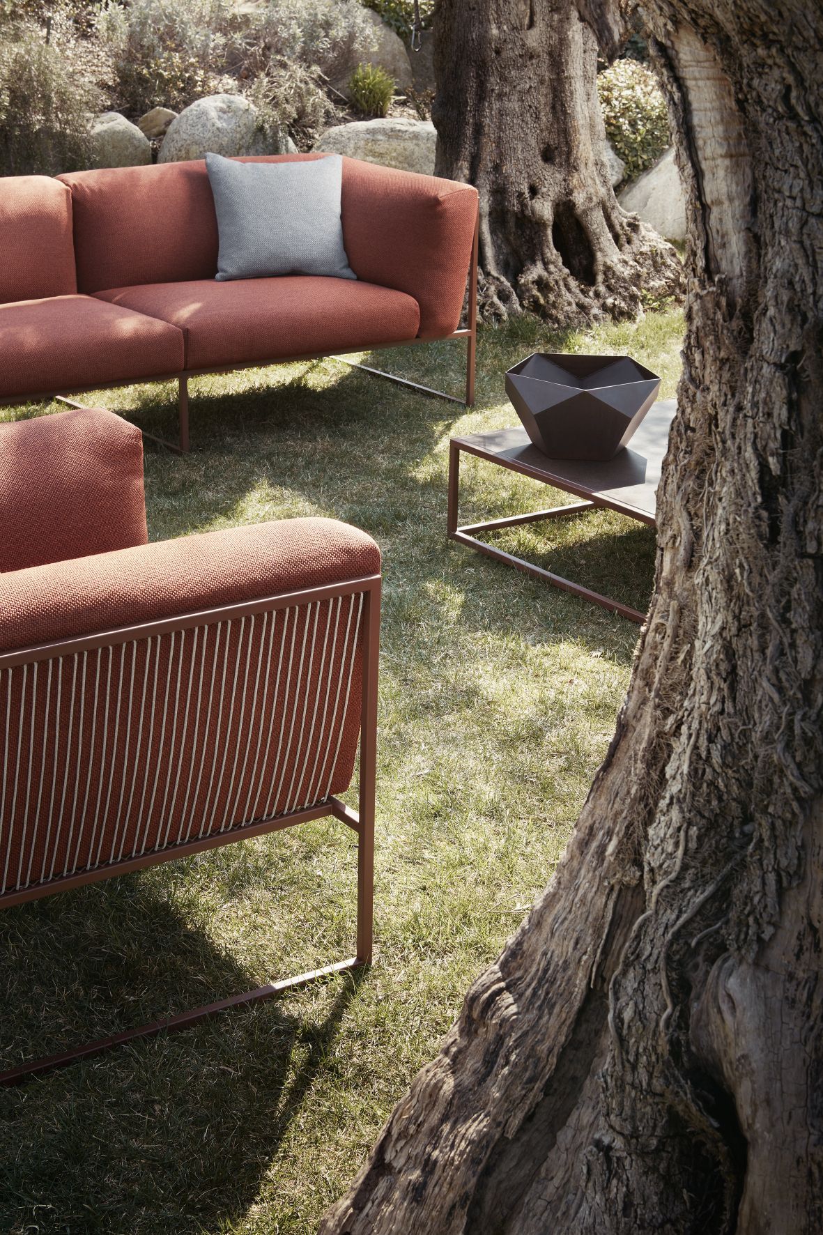 Arpa Sofa von MDF Italia, Outdoor 3-Sitzer in Terrakotta mit grauem Kissen im Garten.