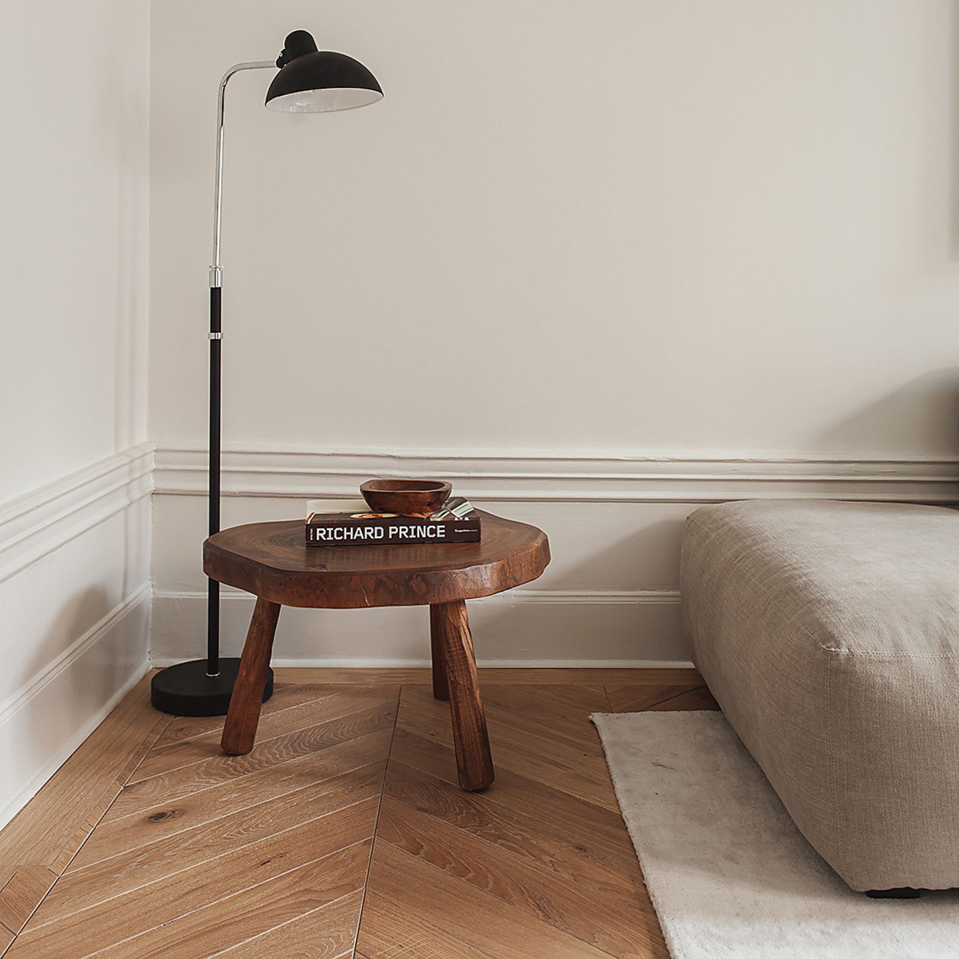 Schwarze KAISER idell Stehleuchte 6580 F von Fritz Hansen neben einem Holzhocker im Interieur.