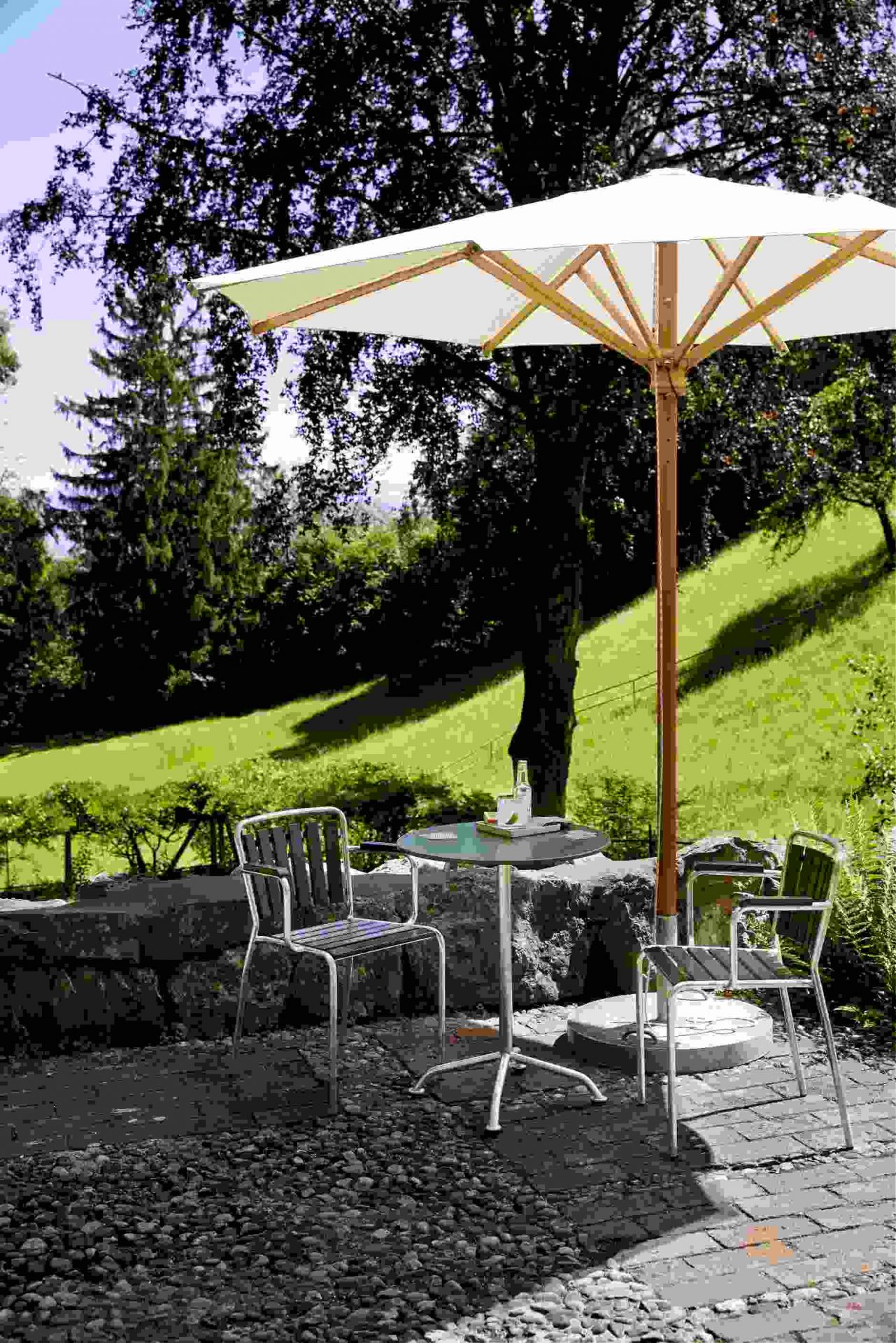 Haefeli Gartentisch Outdoor, Ø 60 cm, unter Sonnenschirm mit Stühlen im Garten. Runder Gartentisch für Terrasse.